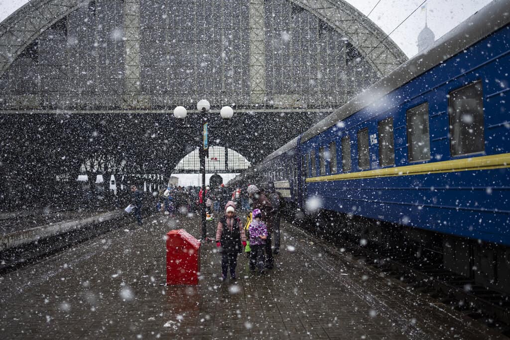Una familia ucraniana espera bajo la nieve abordar un tren en la estación de Lviv, Ucrania, el 27 de febrero del 2022. 
