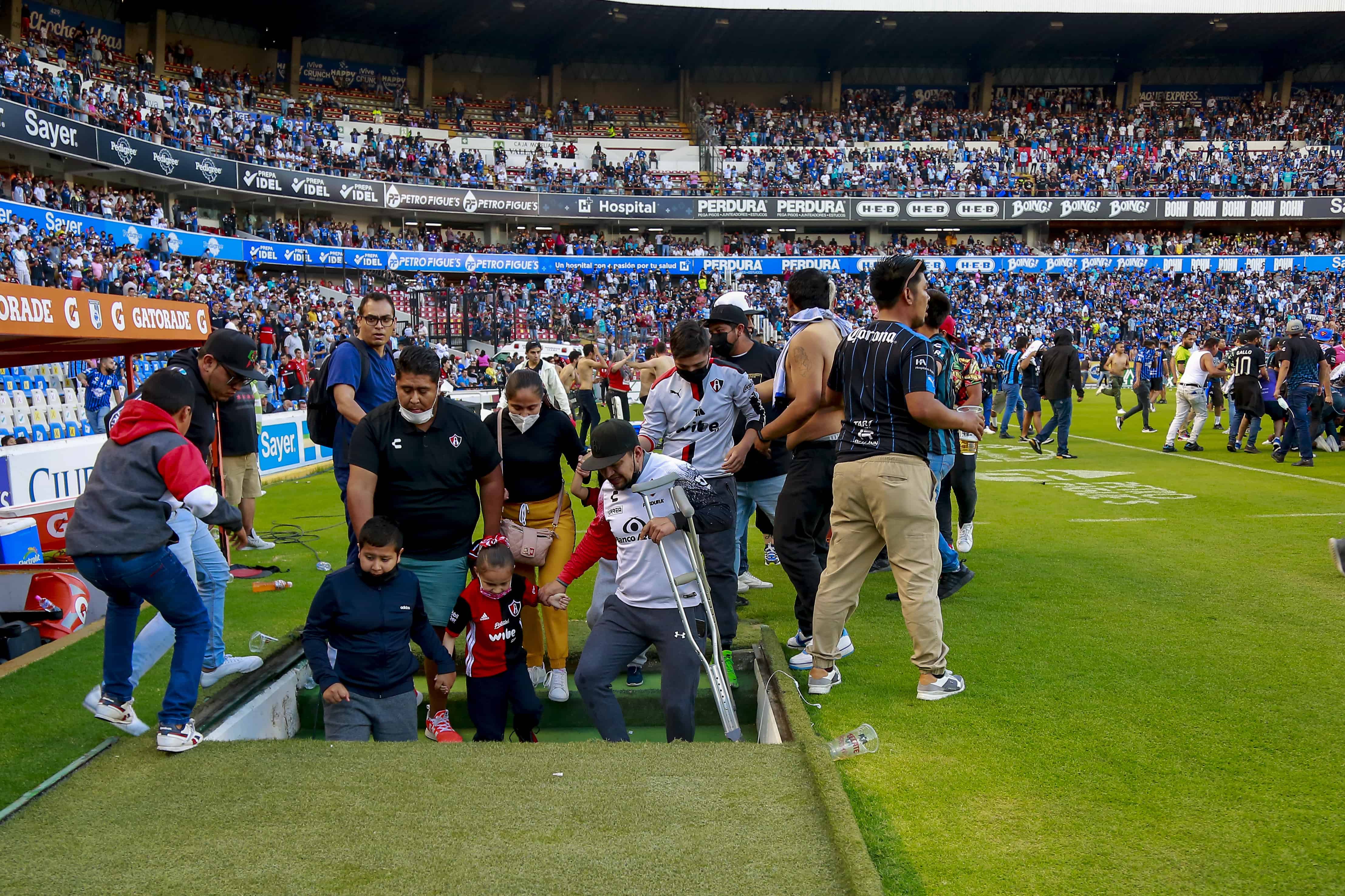 Seguidores del Querétaro y el Atlas descienden a los túneles para protegerse mientras otros aficionados riñen durante un partido que debió suspenderse el sábado 5 de marzo de 2022.