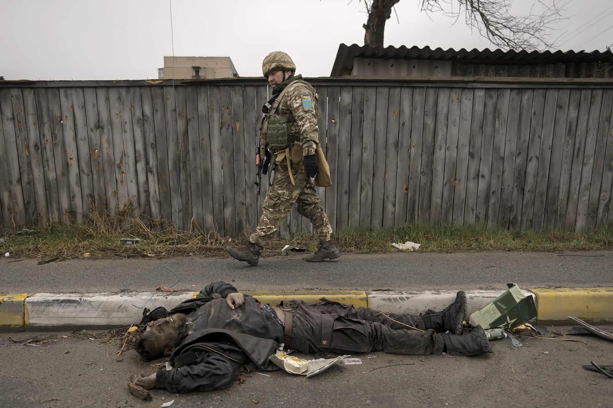Un militar ucraniano camina junto a un cuerpo sin vida tirado en la calle mientras busca trampas explosivas en el suburbio de Bucha, Ucrania, anteriormente ocupado por Rusia, el sábado 2 de abril de 2022.