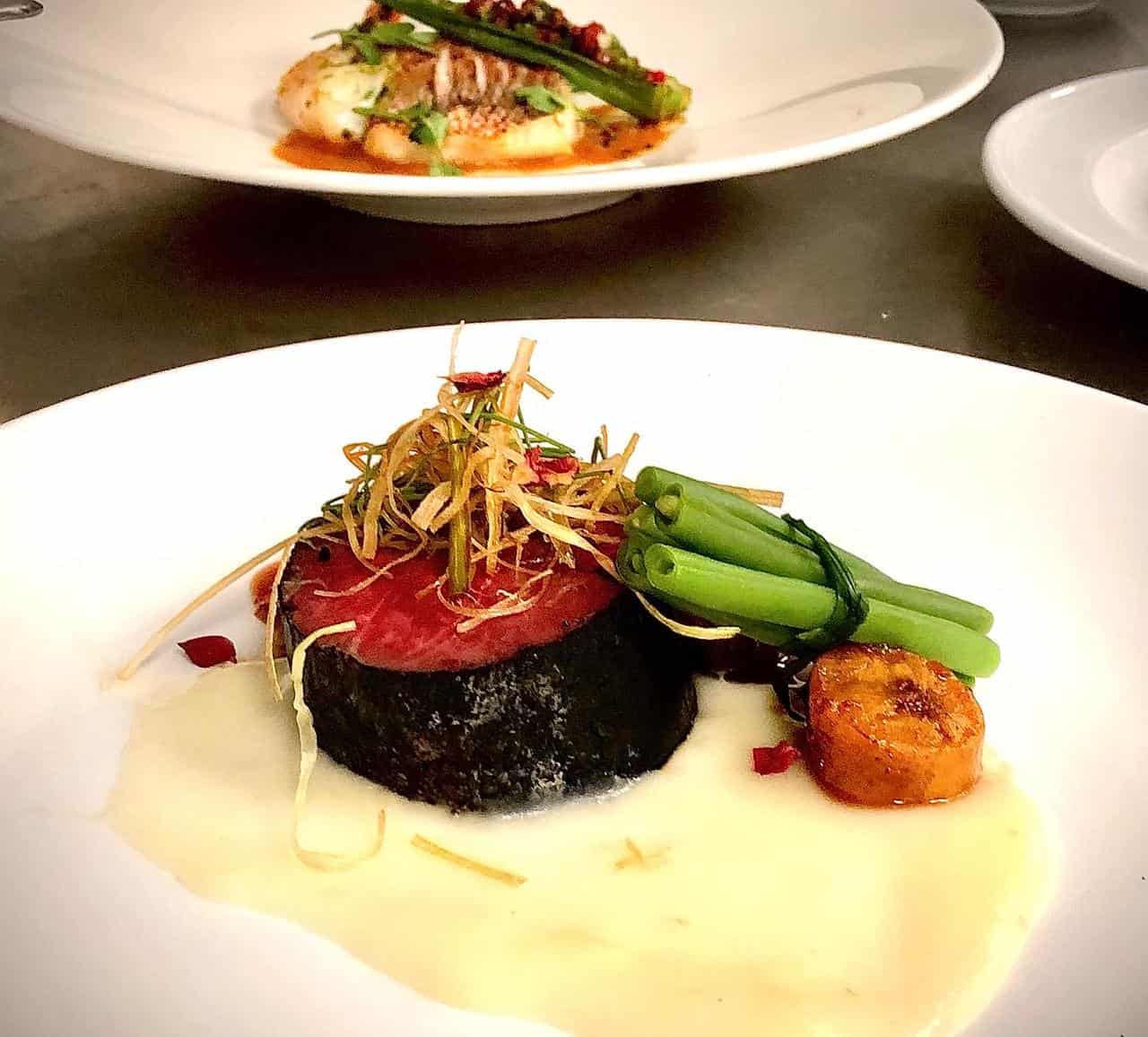 Nuestro beef tenderloin curado en mamajuana seca y kahkow 82%, muselina de yuca, plátano maduro al caldero, atado de vainitas y jus a la perigourd.