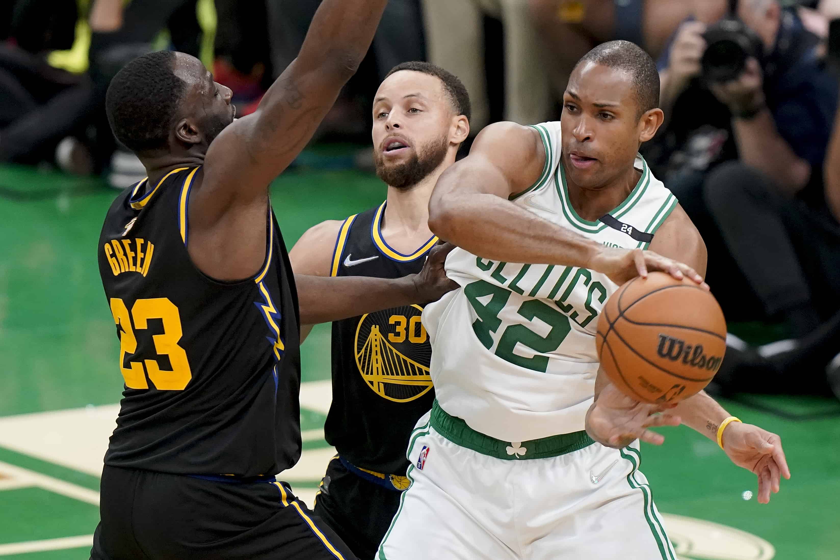 El centro de los Boston Celtics, Al Horford (42), pasa el balón contra el escolta de los Golden State Warriors, Stephen Curry (30) y el alero Draymond Green (23), durante el segundo cuarto del Juego 3 de las Finales de la NBA, el miércoles 8 de junio de 2022 en Boston. 