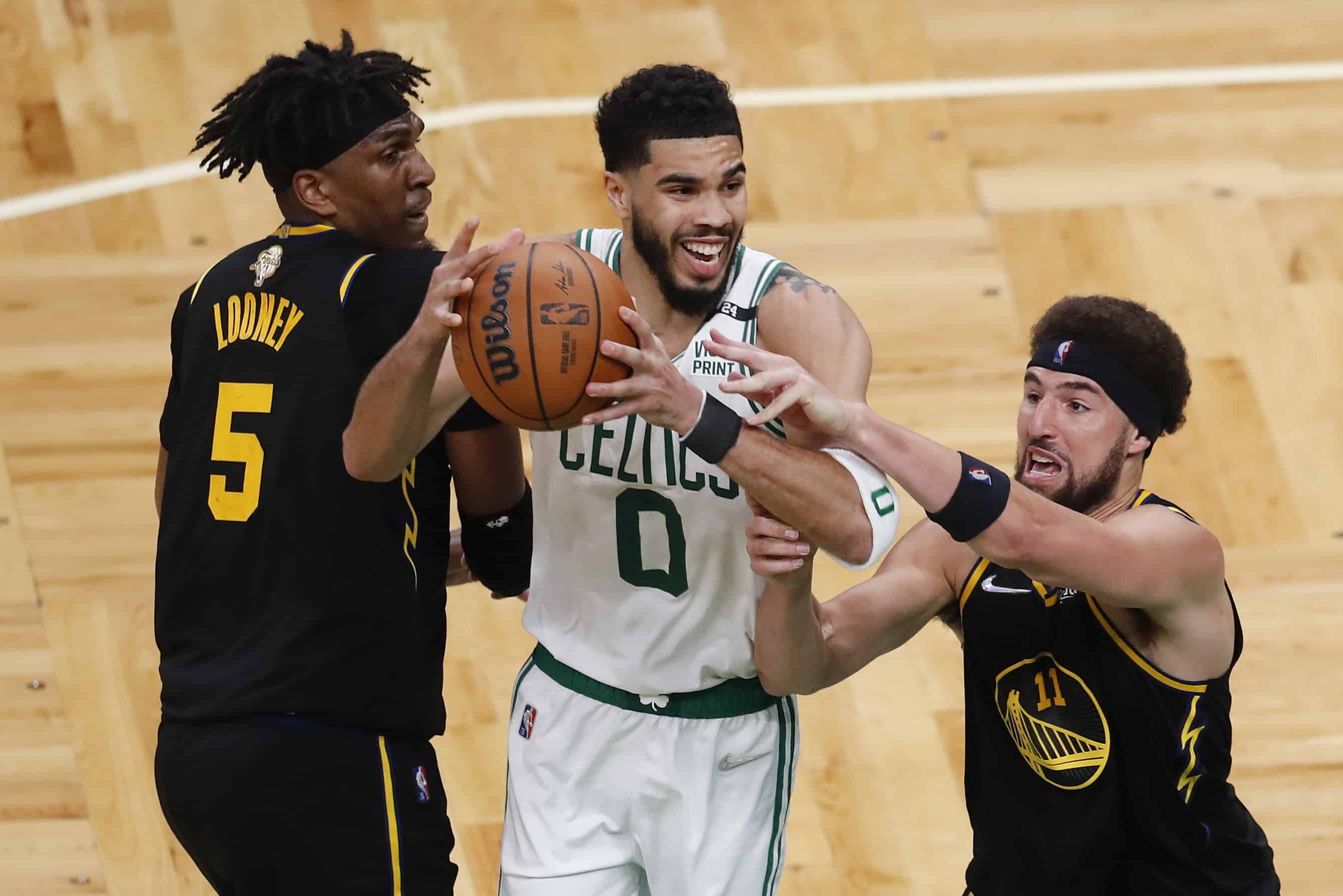 El alero de los Boston Celtics, Jayson Tatum (0), lucha por un rebote contra el centro de los Golden State Warriors, Kevon Looney (5), y el guardia Klay Thompson (11), durante el último cuarto del Juego 3 de las Finales de la NBA de baloncesto, el miércoles 8 de junio de 2022 en Boston. . 