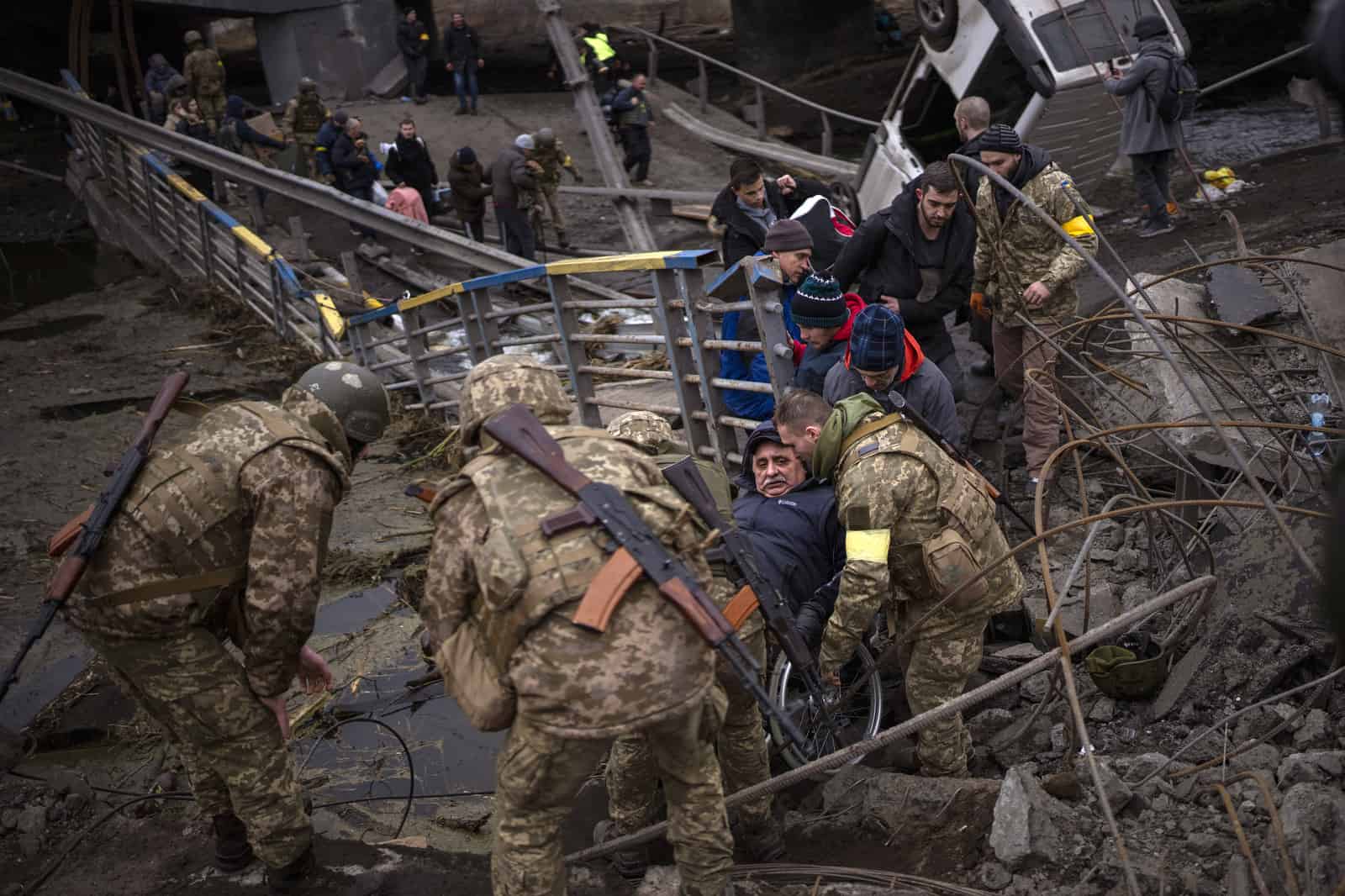 ARCHIVO - Soldados ucranianos ayudan a un hombre en silla de ruedas mientras la gente trata de huir cruzando el río Irpin en las afueras de Kiev, Ucrania, el sábado 5 de marzo de 2022.