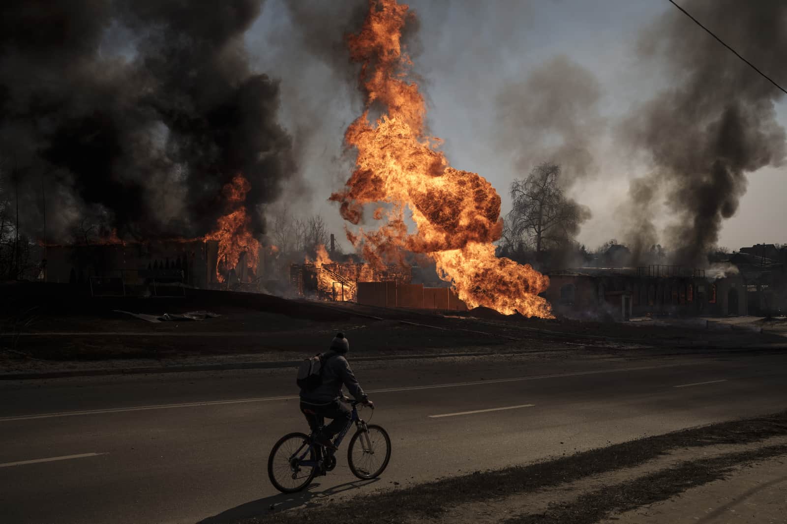 ARCHIVO - Un hombre monta su bicicleta frente a las llamas y el humo que sale de un incendio luego de un ataque ruso en Kharkiv, Ucrania, el 25 de marzo de 2022.