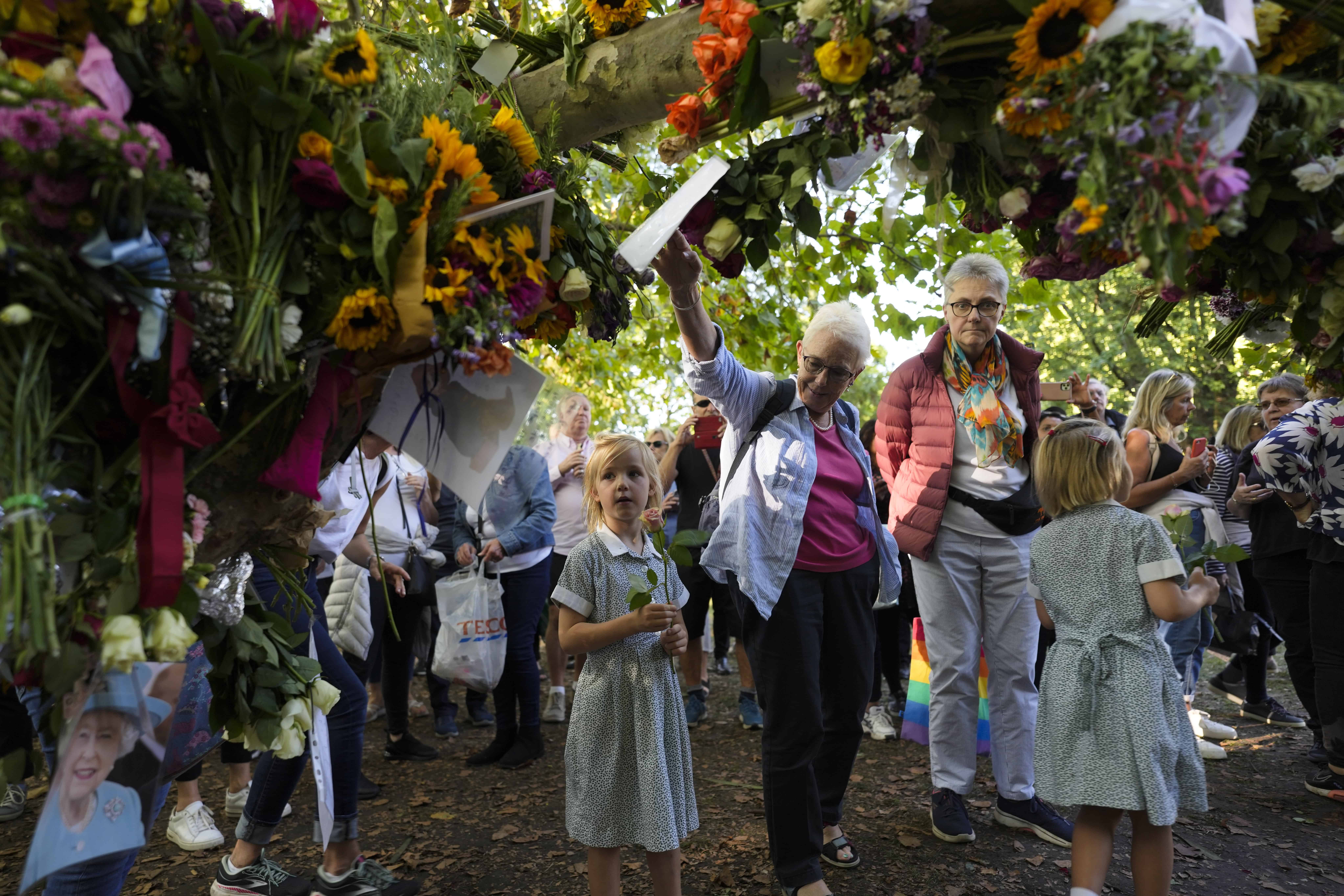 La gente se para junto a las flores y los mensajes colocados en la rama de un árbol para la reina Isabel II, en el memorial de Green Park junto al Palacio de Buckingham en Londres
