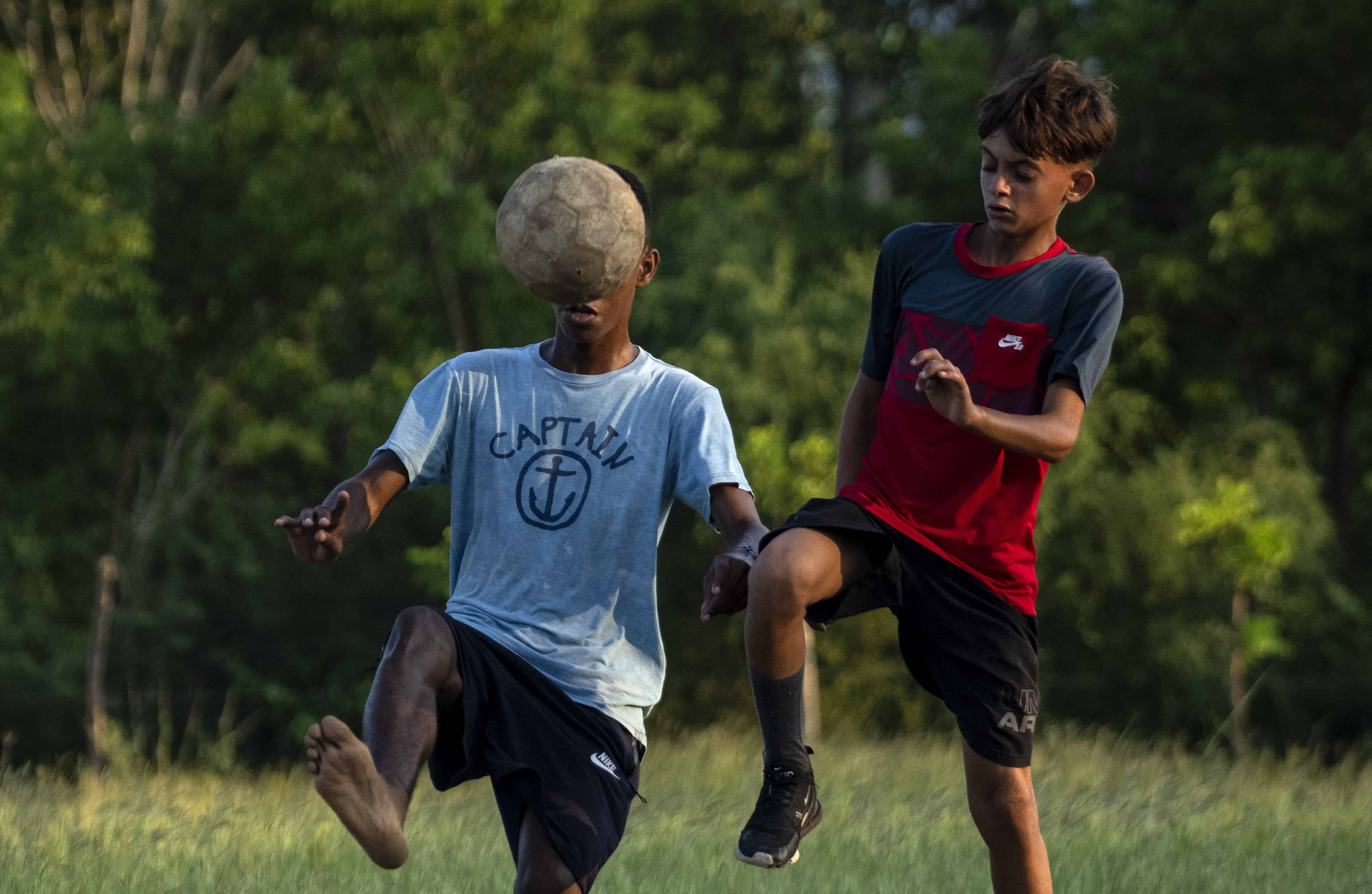 Dos chicos, uno de ellos descalzo, se disputan un viejo balón durante un partido de fútbol en un antiguo campo de béisbol en Guanabacoa (Cuba) el 15 de octubre del 2022.&nbsp;