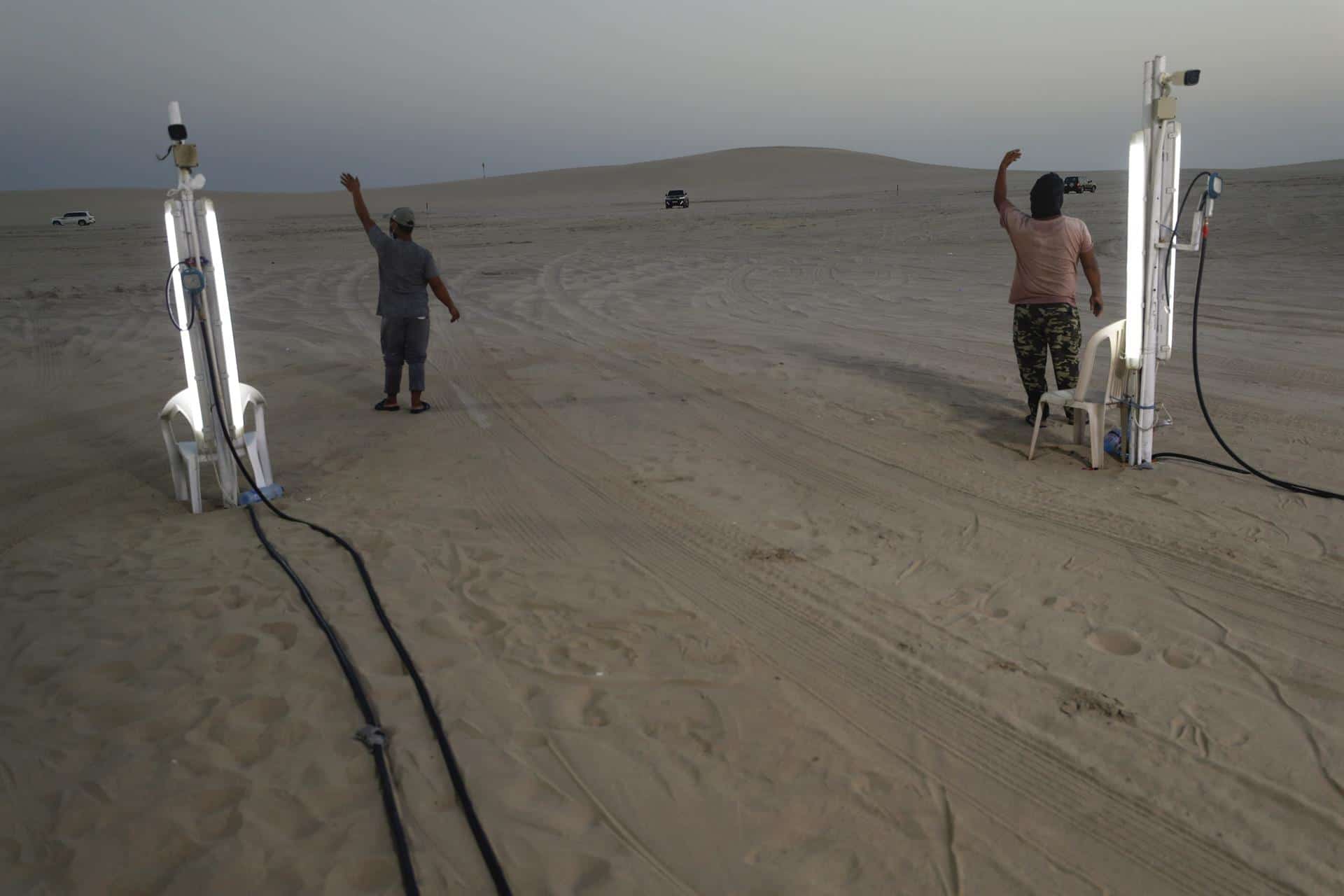 Dos trabajadores intentan captar clientes en la estación de inflado de ruedas situado en la salida del desierto de Catar.<br>