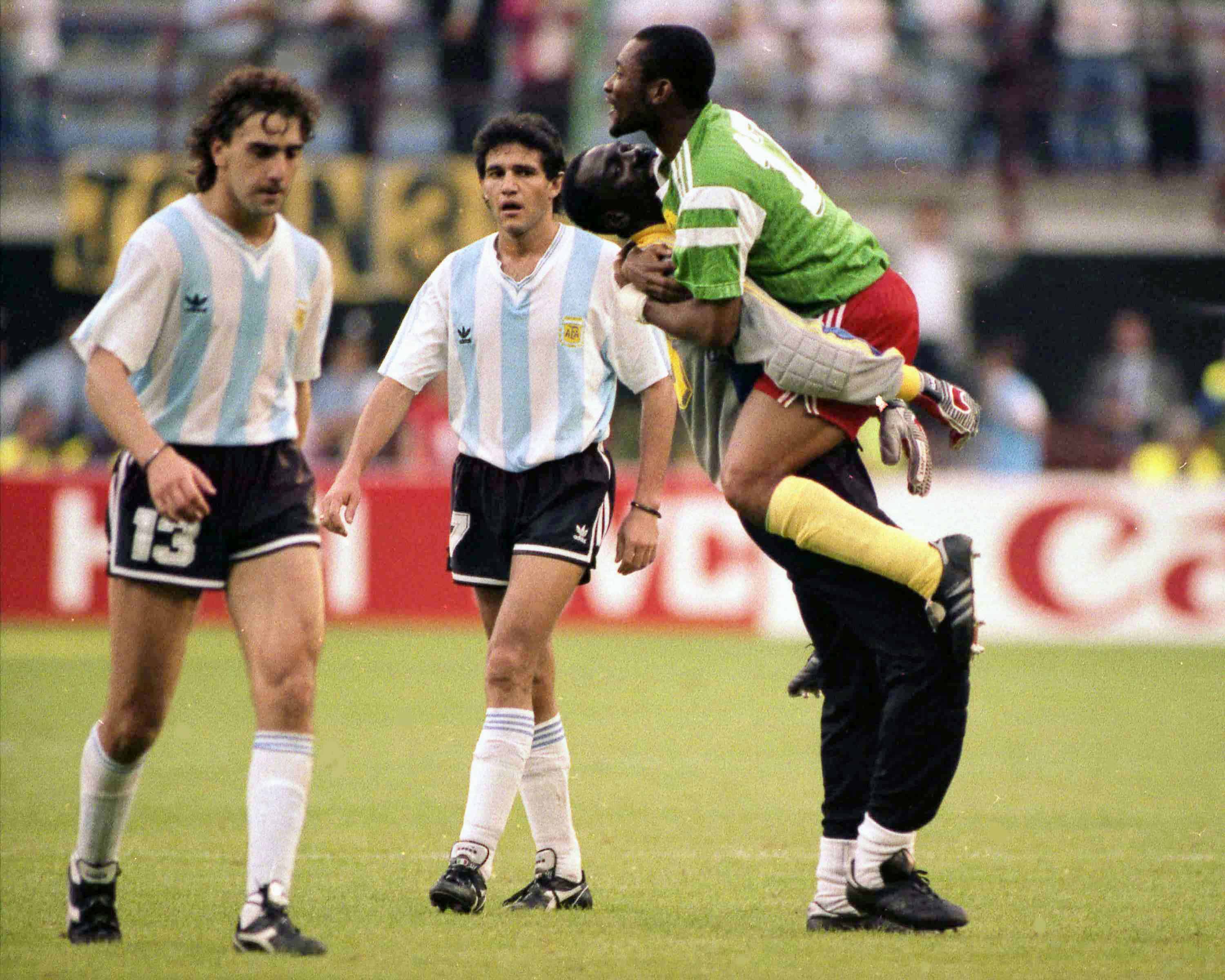 Los abatidos jugadores argentinos Néstor Gabriel Lorenzo, a la izquierda, y Jorge Luis Burruchaga salen de la cancha, pasan junto a jugadores cameruneses que celebran, después del partido inaugural de la Copa Mundial de fútbol,  en Milán, Italia, el 8 de junio de 1990. Camerún derrotó al campeón defensor Argentina 1-0 en 1990.