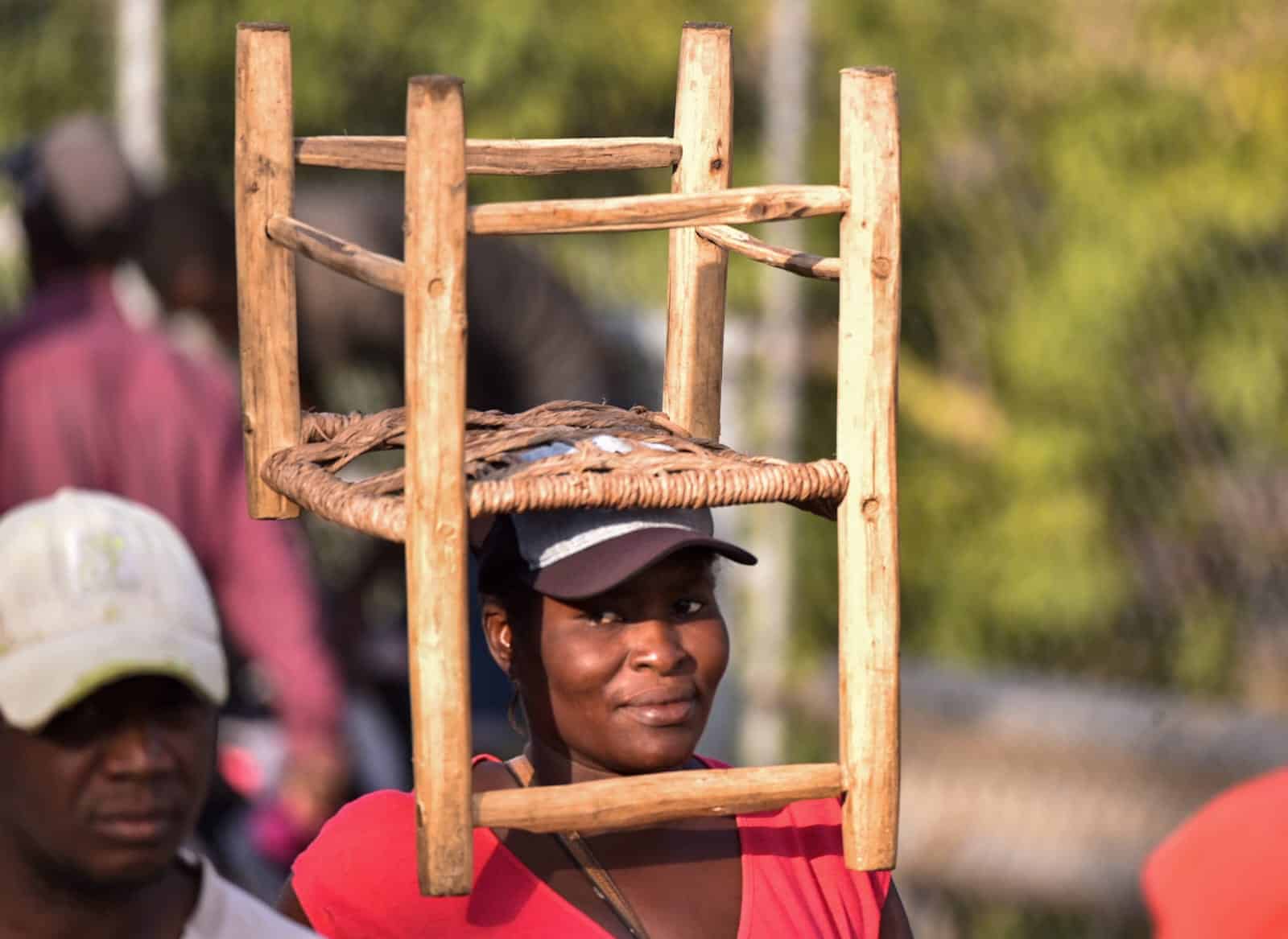 Una mujer haitiana carga una silla en la cabeza, mientras entra al mercado.<br>