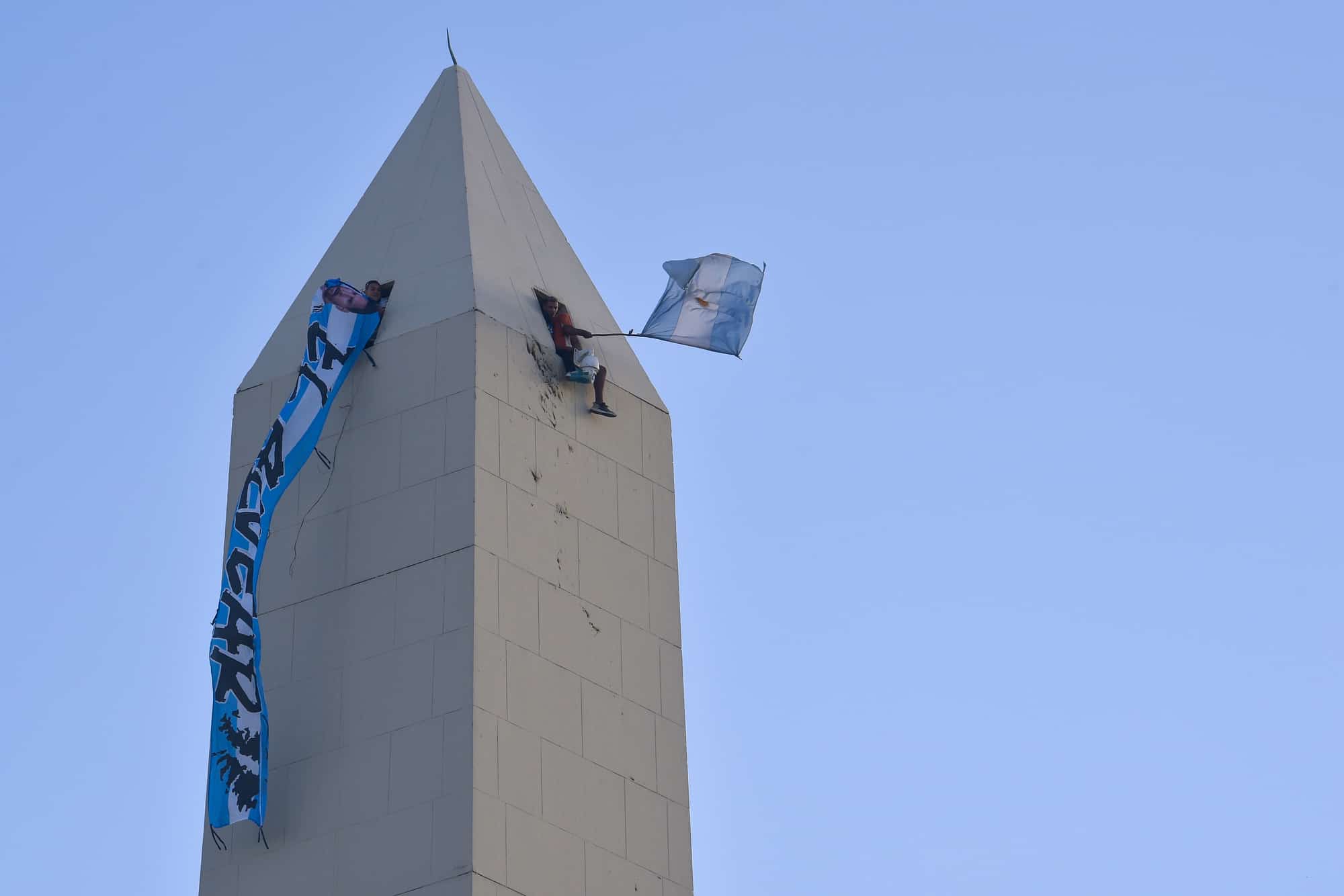 Hinchas argentinos agitan banderas desde la parte superior del obelisco mientras esperan a la selección de su país, campeona del mundo, en Buenos Aires, el martes 20 de diciembre de 2022