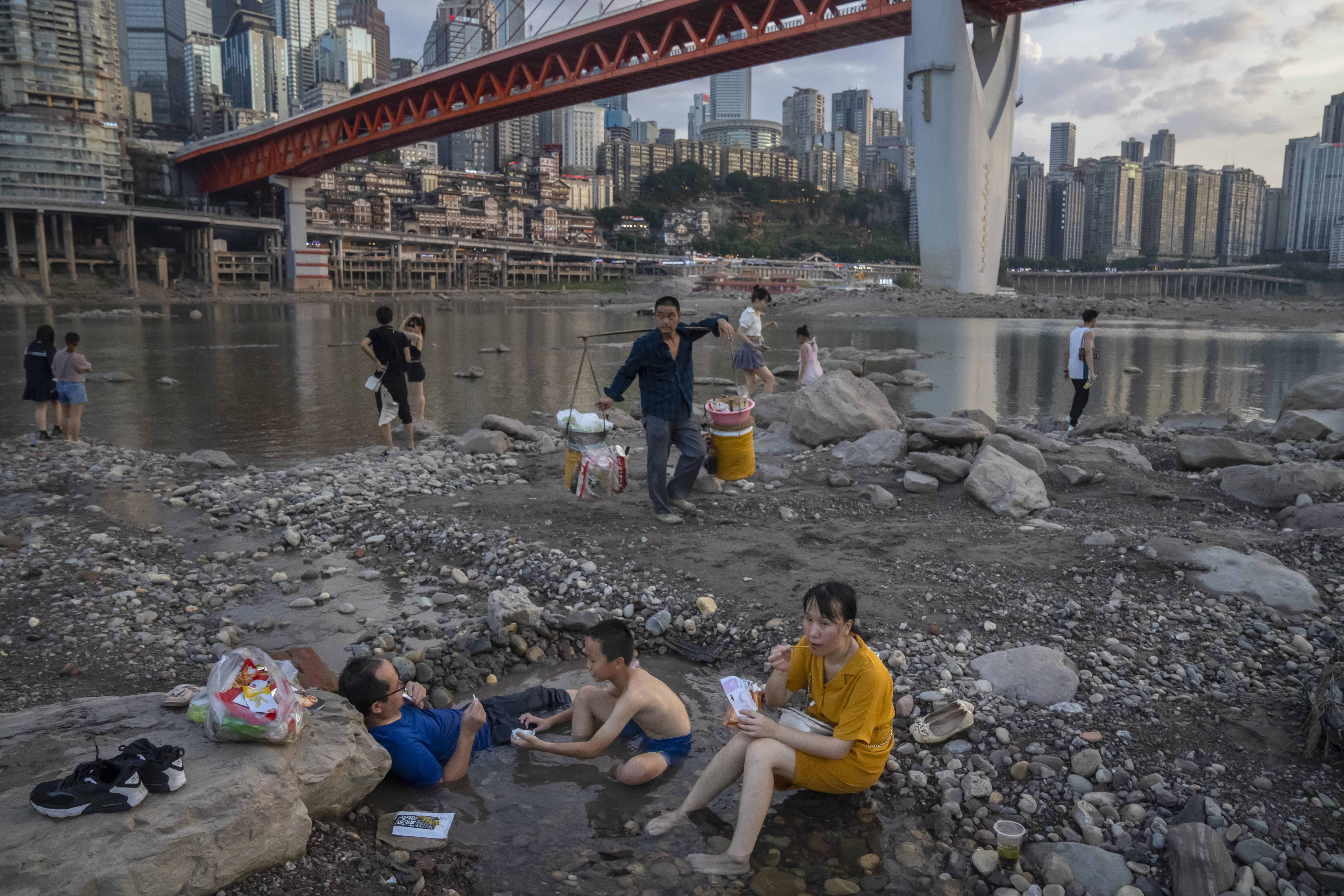 La gente se sienta en un charco de agua poco profundo en el lecho del río Jialing, un afluente del Yangtze, en la municipalidad de Chongqing, suroeste de China, el sábado 20 de agosto de 2022. El paisaje mismo de Chongqing, una megaciudad que también abarca las tierras de cultivo circundantes y montañas empinadas y pintorescas, ha sido transformada por una ola de calor inusualmente larga e intensa y la sequía que la acompaña.