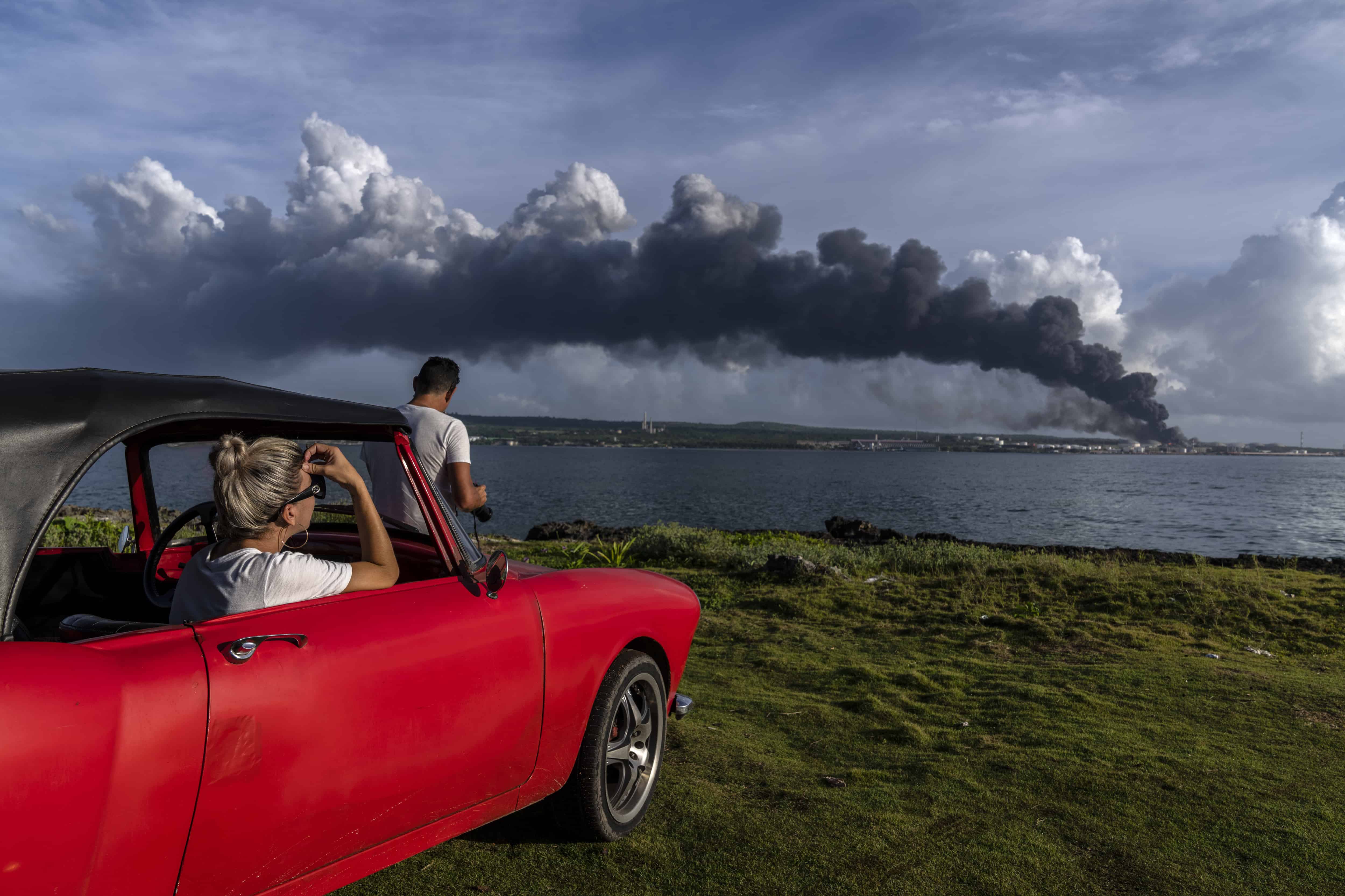 ersonas mirando la columna de humo que se eleva desde la base de supertanqueros de Matanzas en la que un rayo inició un incendio mortal durante una tormenta la noche anterior en Matanzas, Cuba, el domingo 7 de agosto de 2022. Las llamas forzaron a las autoridades a evacuar a más de 4.900 personas y provocaron la muerte de dos bomberos y 130 heridos y destruyeron cuatro de los ocho tanques de la instalación.