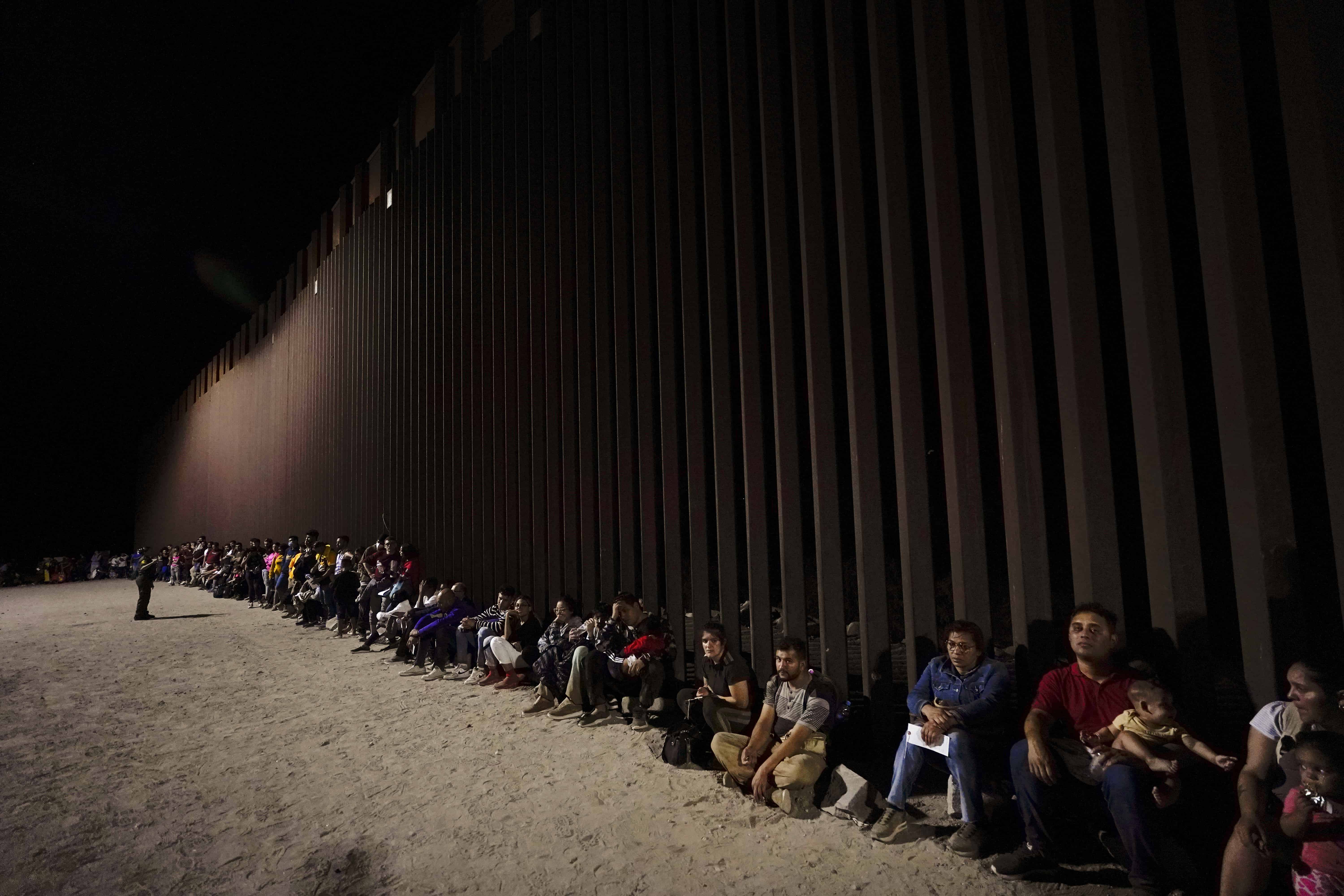 Migrantes esperan a lo largo del muro fronterizo después de cruzar desde México, cerca de Yuma, Ariz, el martes 23 de agosto de 2022.