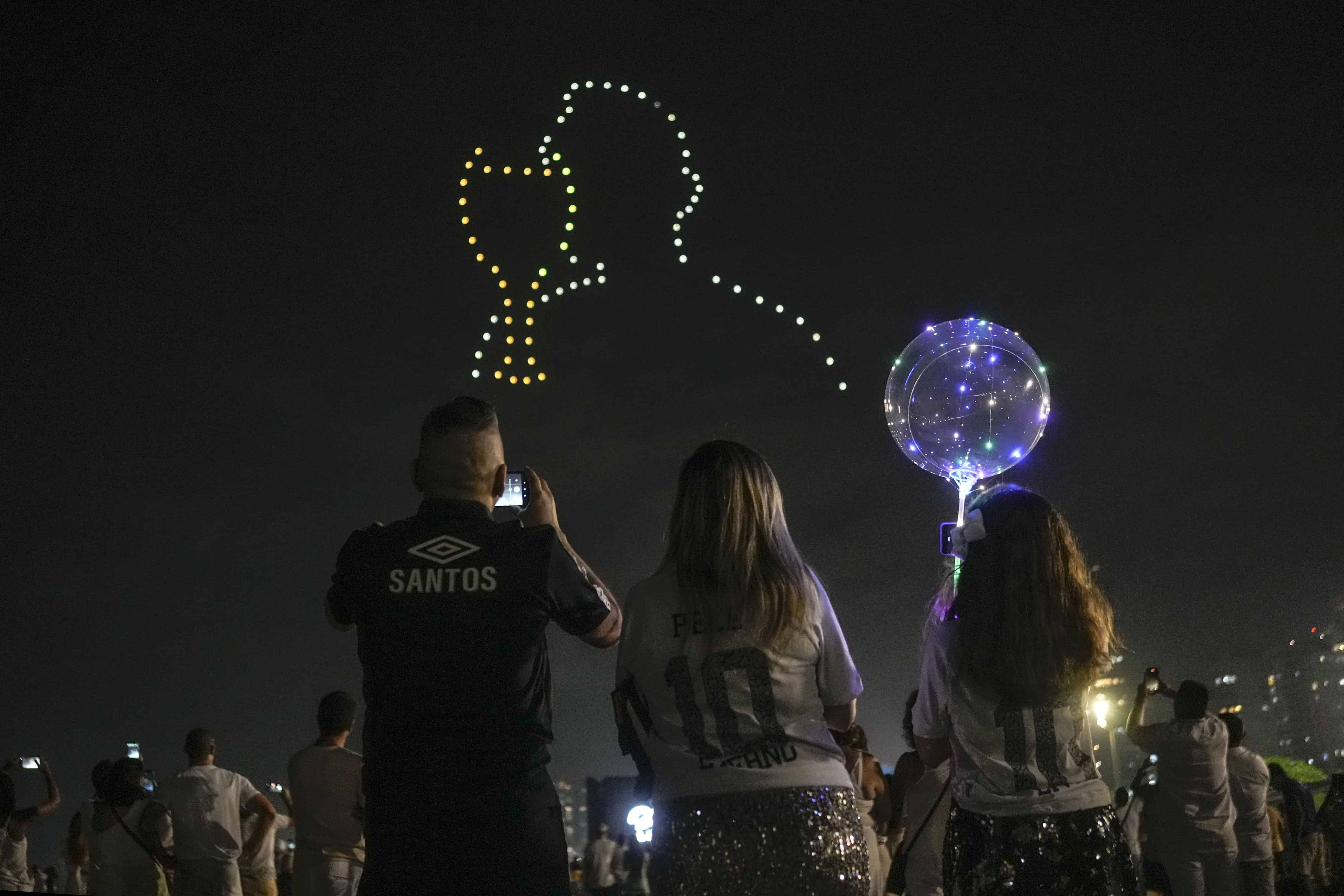La gente mira un espectáculo de drones en homenaje a la fallecida estrella del fútbol brasileño Pelé, sobre la playa de Gonzaga en Santos, Brasil, el sábado 31 de diciembre de 2022. Pelé, quien jugó la mayor parte de su carrera con Santos, murió en Sao Paulo el jueves en el 82 años. 