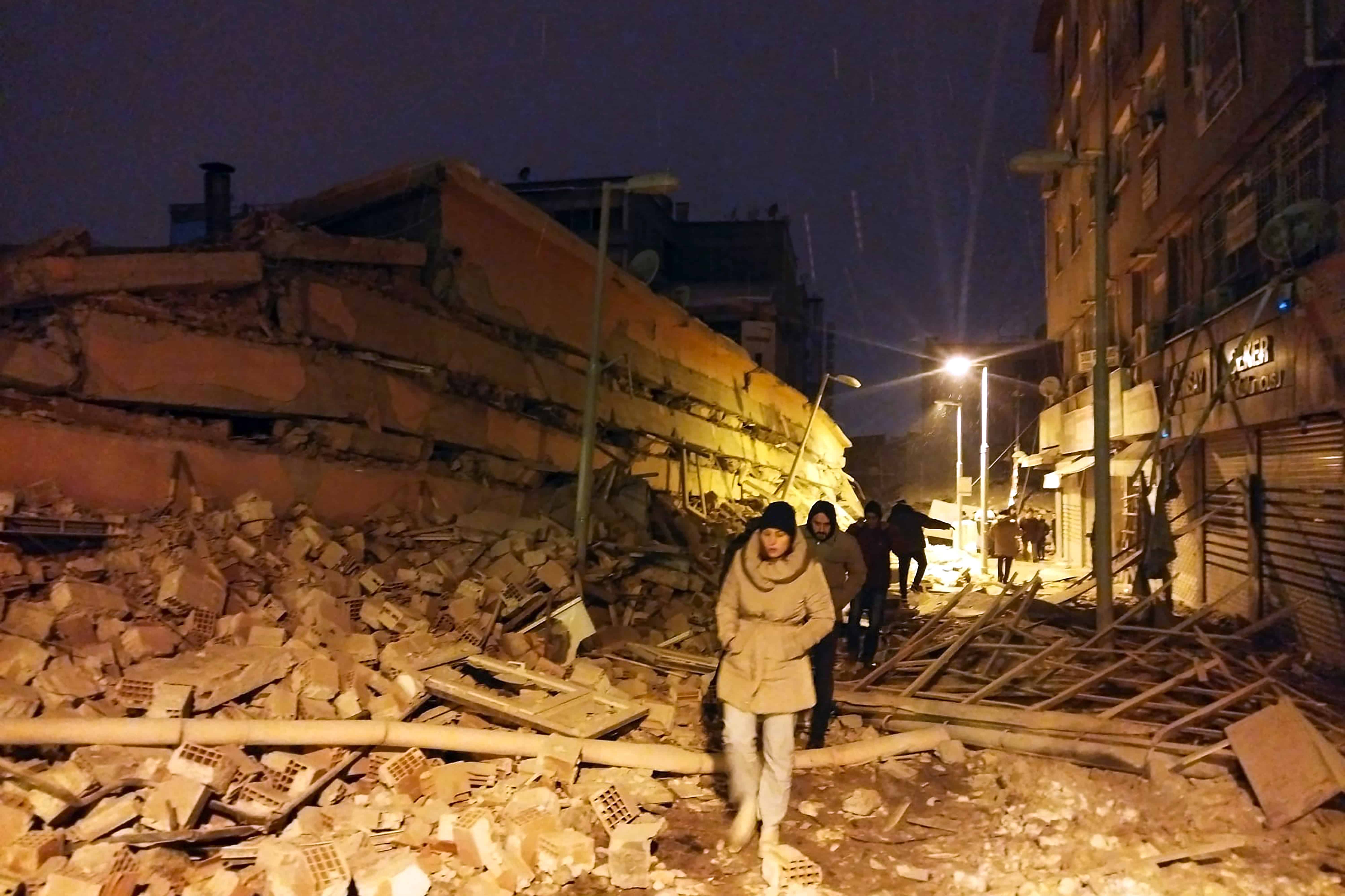 Personas caminan junto a edificios destruidos por un terremoto en Malatya, Turquía, el lunes 6 de febrero de 2023. Un poderoso sismo derribó varios edificios en el sureste de Turquía y Siria y se temen muchas víctimas.