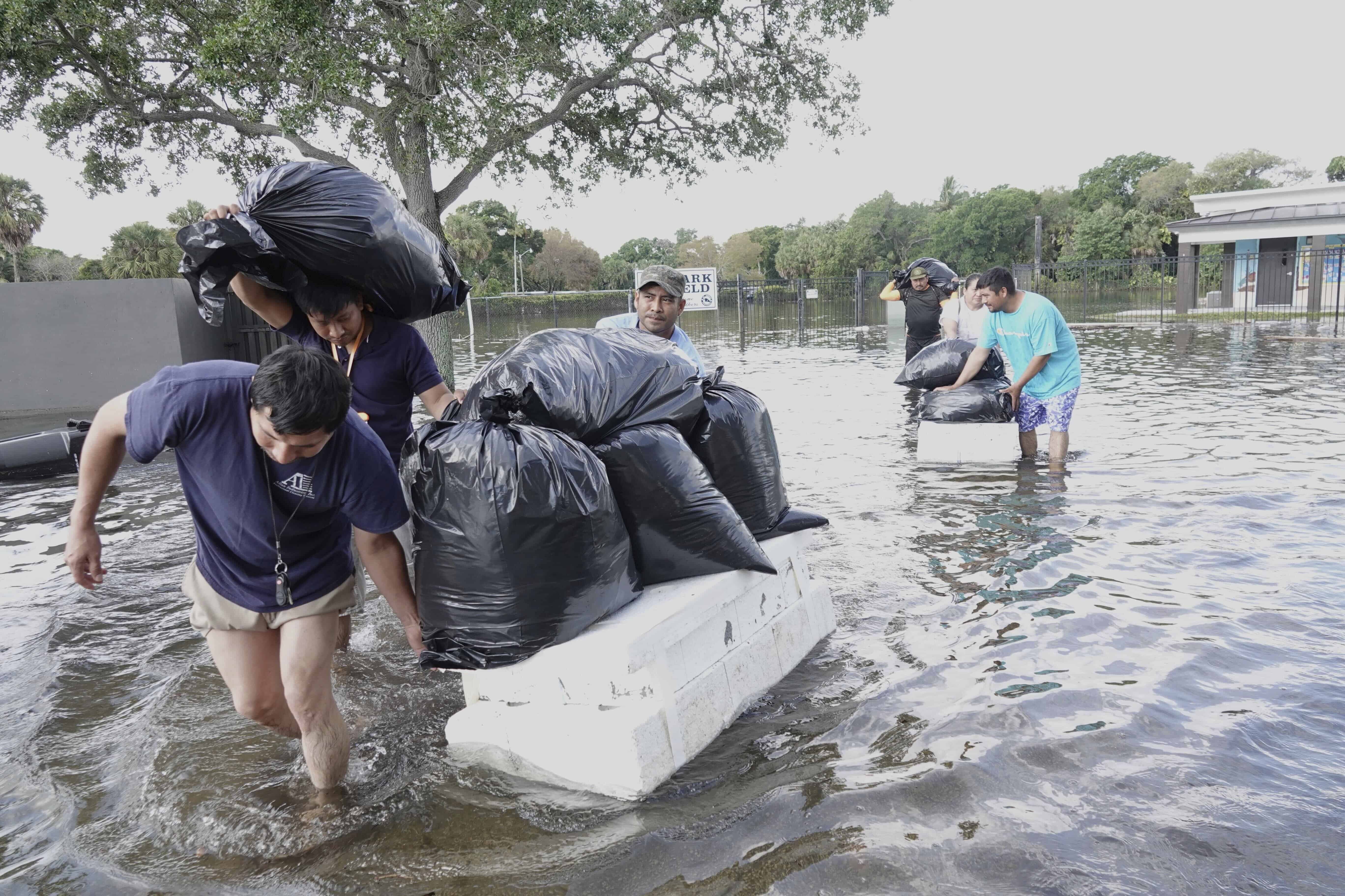 La gente trata de salvar objetos de valor, caminando a través de las aguas de las inundaciones en un vecindario de Fort Lauderdale, Florida, el jueves 13 de abril de 2023.