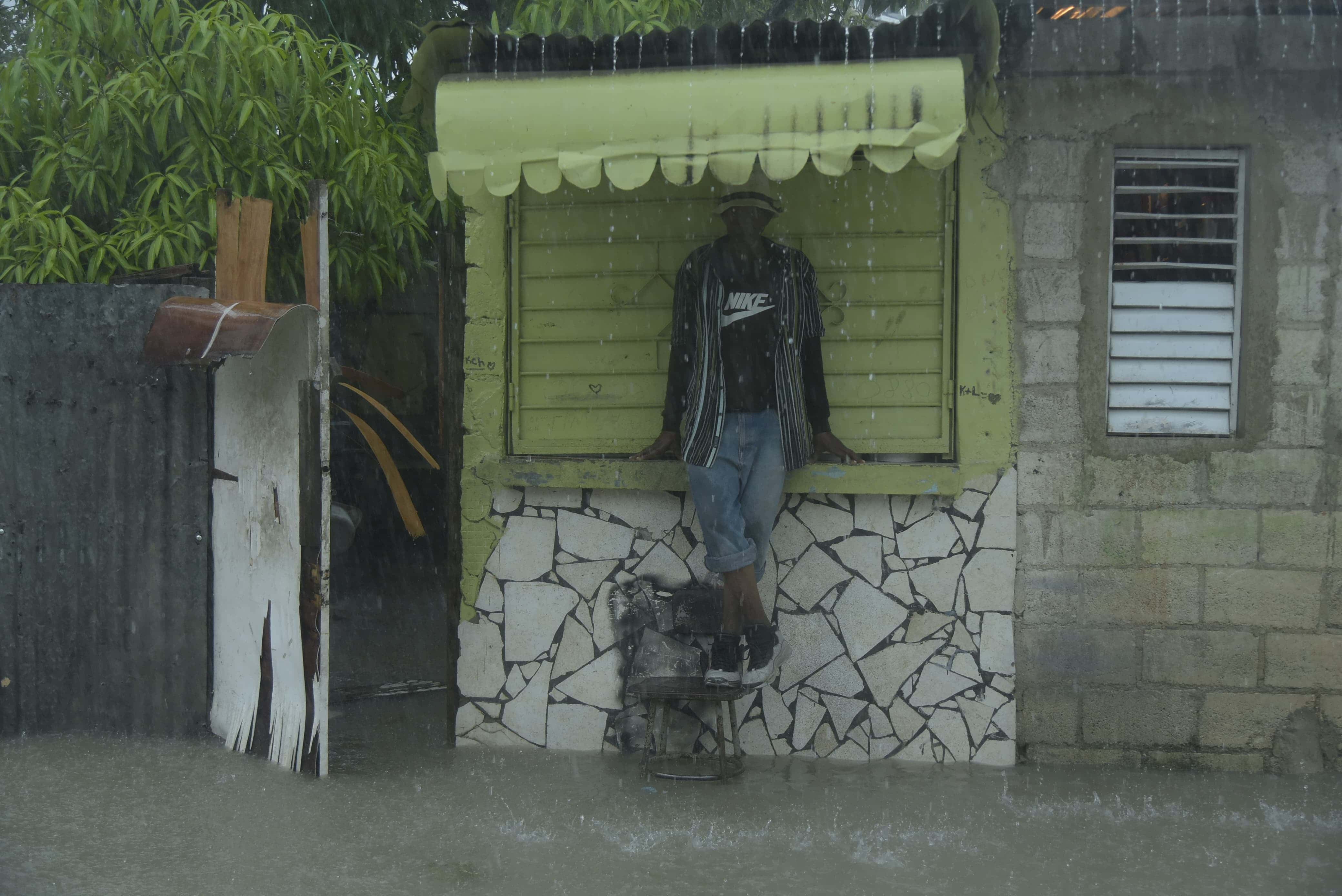 Esperar bajo la lluvia y con los pies en alto fue la única opción de un joven en el sector Ramón Santana en San Pedro de Macorís.