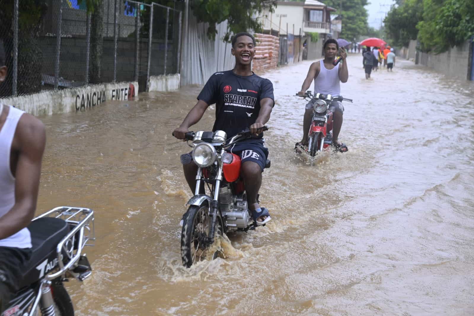 Jóvenes motoristas cruzan calles inundadas en Haina.