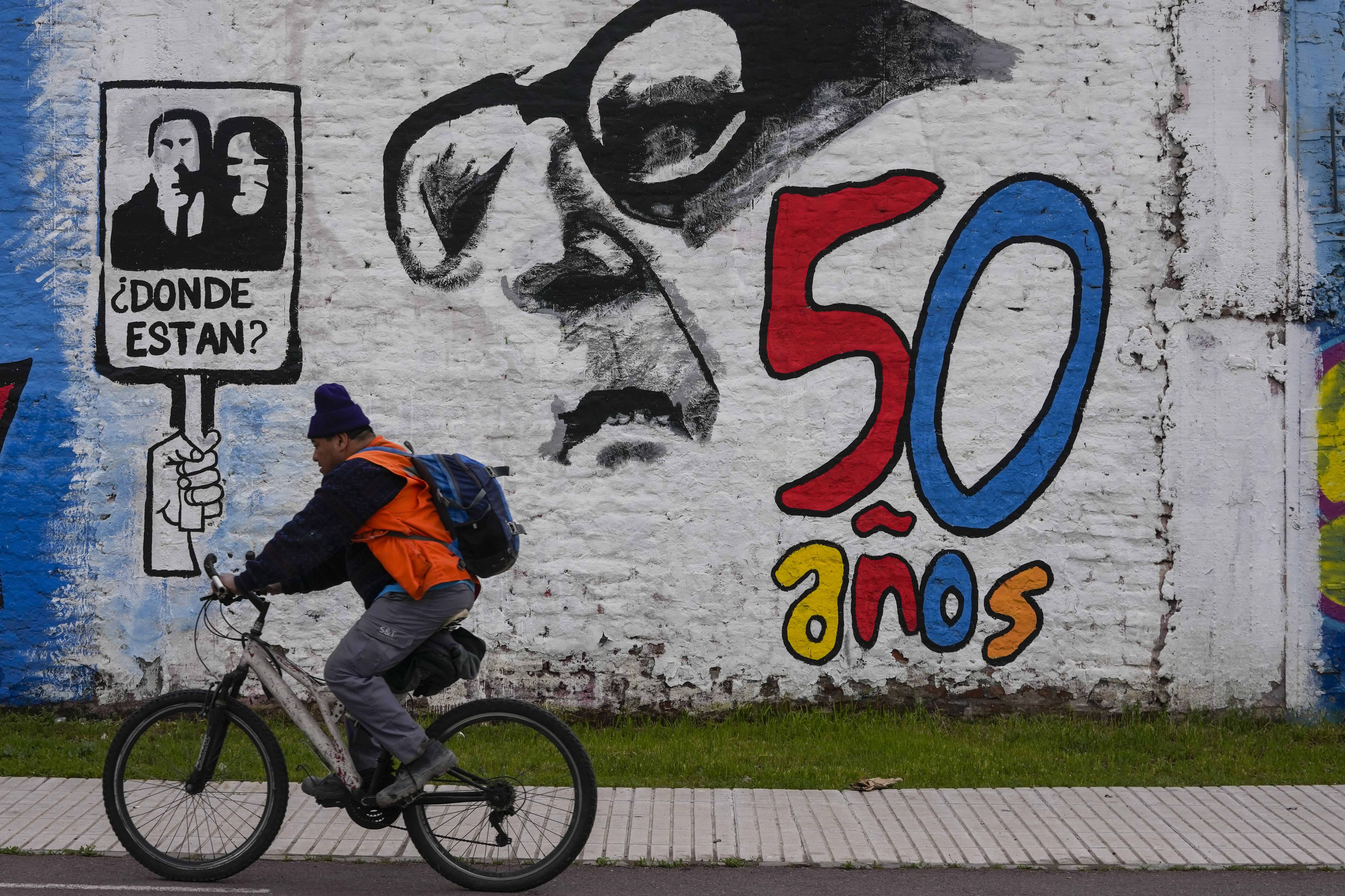 Un hombre pedalea su bicicleta frente a un mural que marca el 50 aniversario del golpe militar del país, con un recordatorio de los desaparecidos durante el régimen de Augusto Pinochet y una imagen que representa al depuesto presidente Salvador Allende, en Santiago, Chile, el viernes 8 de septiembre. 2023.