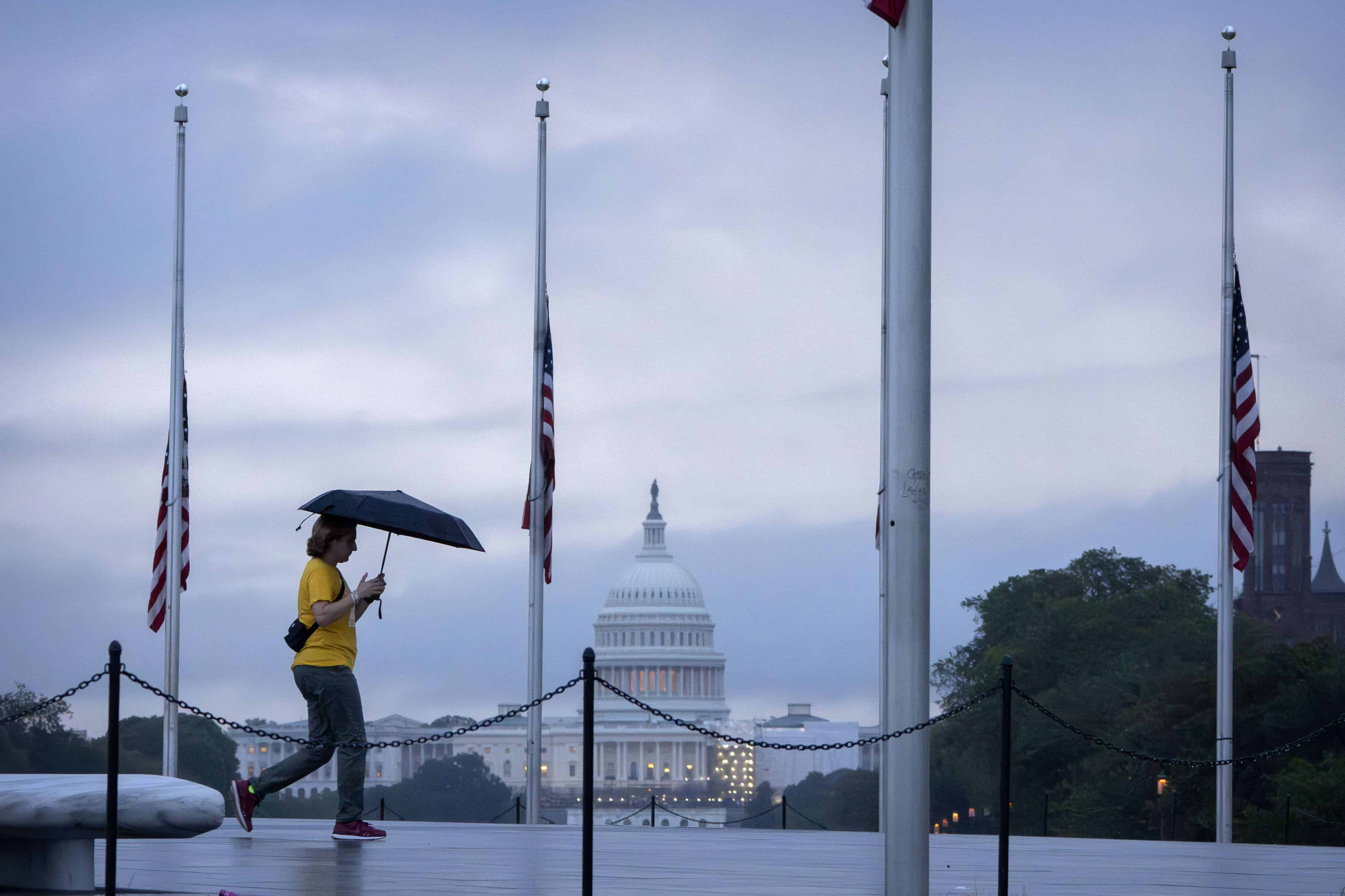 Con el Capitolio de los Estados Unidos al fondo, una persona lleva un paraguas el lunes 11 de septiembre de 2023 en Washington, mientras pasa junto a banderas estadounidenses ondeando a media asta que rodean el Monumento a Washington para honrar y recordar a las víctimas del atentado del 1 de septiembre de 2023. 11 de noviembre de 2001, ataque terrorista.