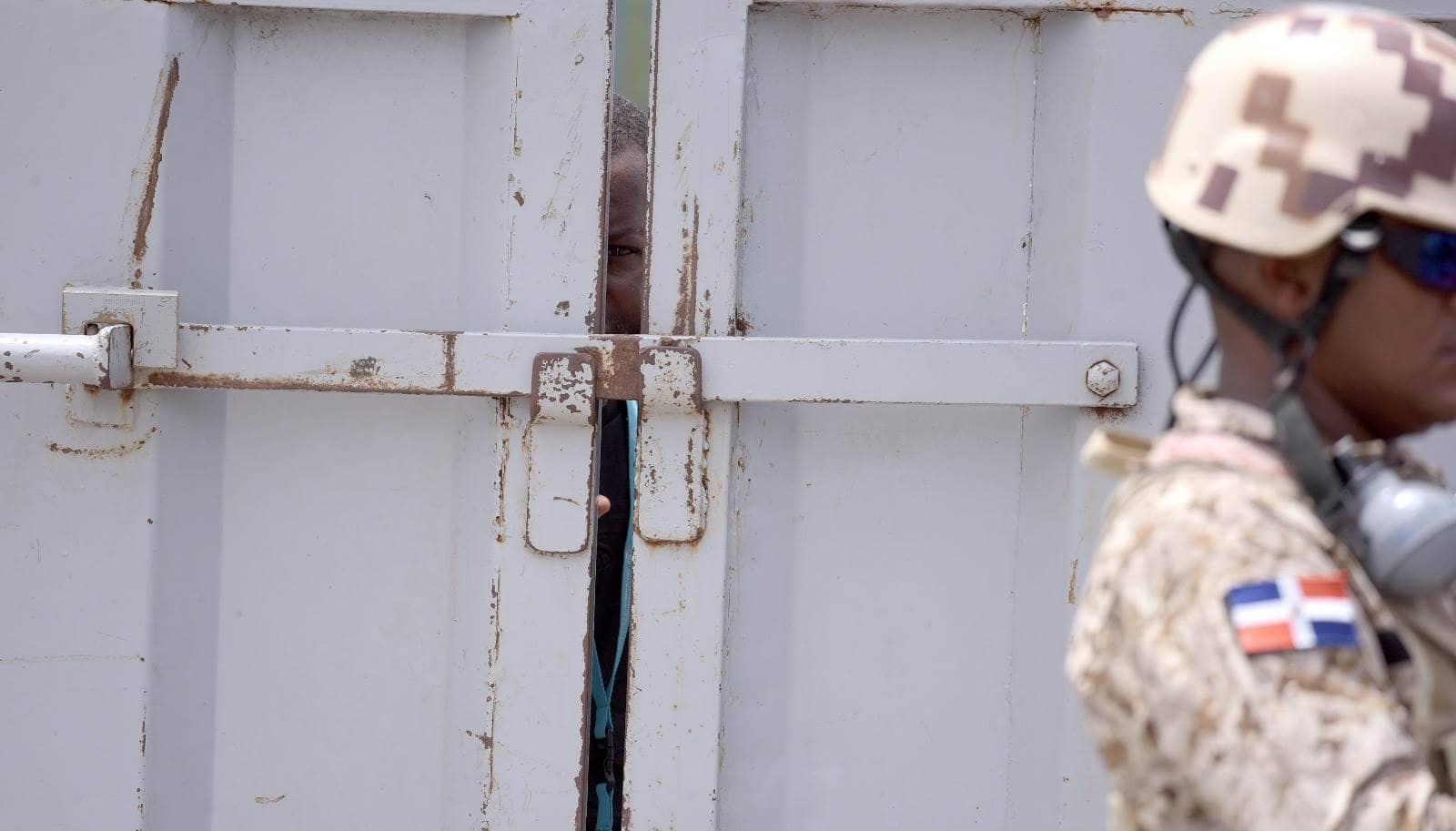 Un ciudadano haitiano observa a través de la puerta fronteriza custodiada por un guardia dominicano.