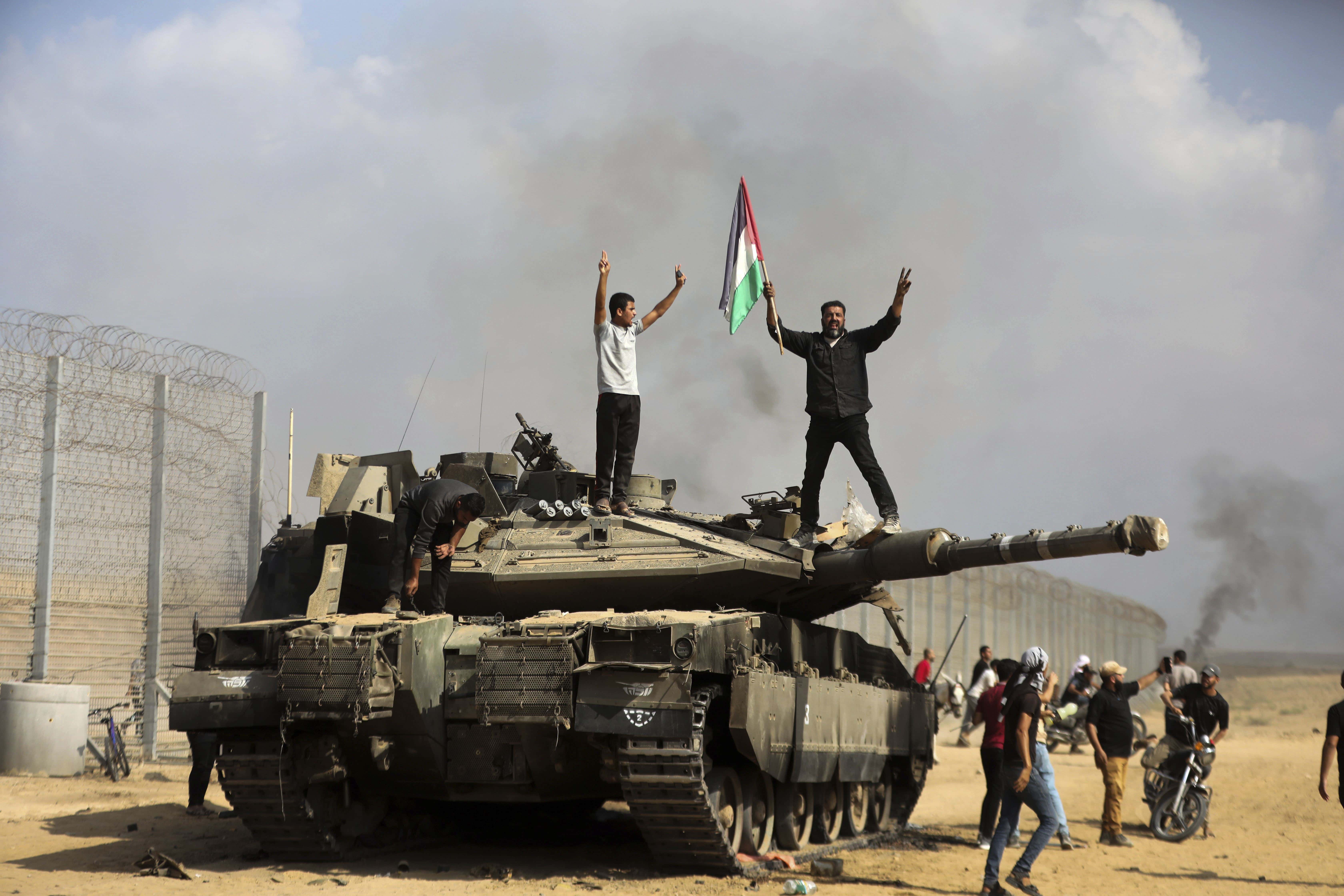 Palestinos ondean una bandera nacional y celebran junto a un tanque israelí destruido en la valla fronteriza que separa la Franja de Gaza de Israel, al este de Khan Younis, el 7 de octubre de 2023.