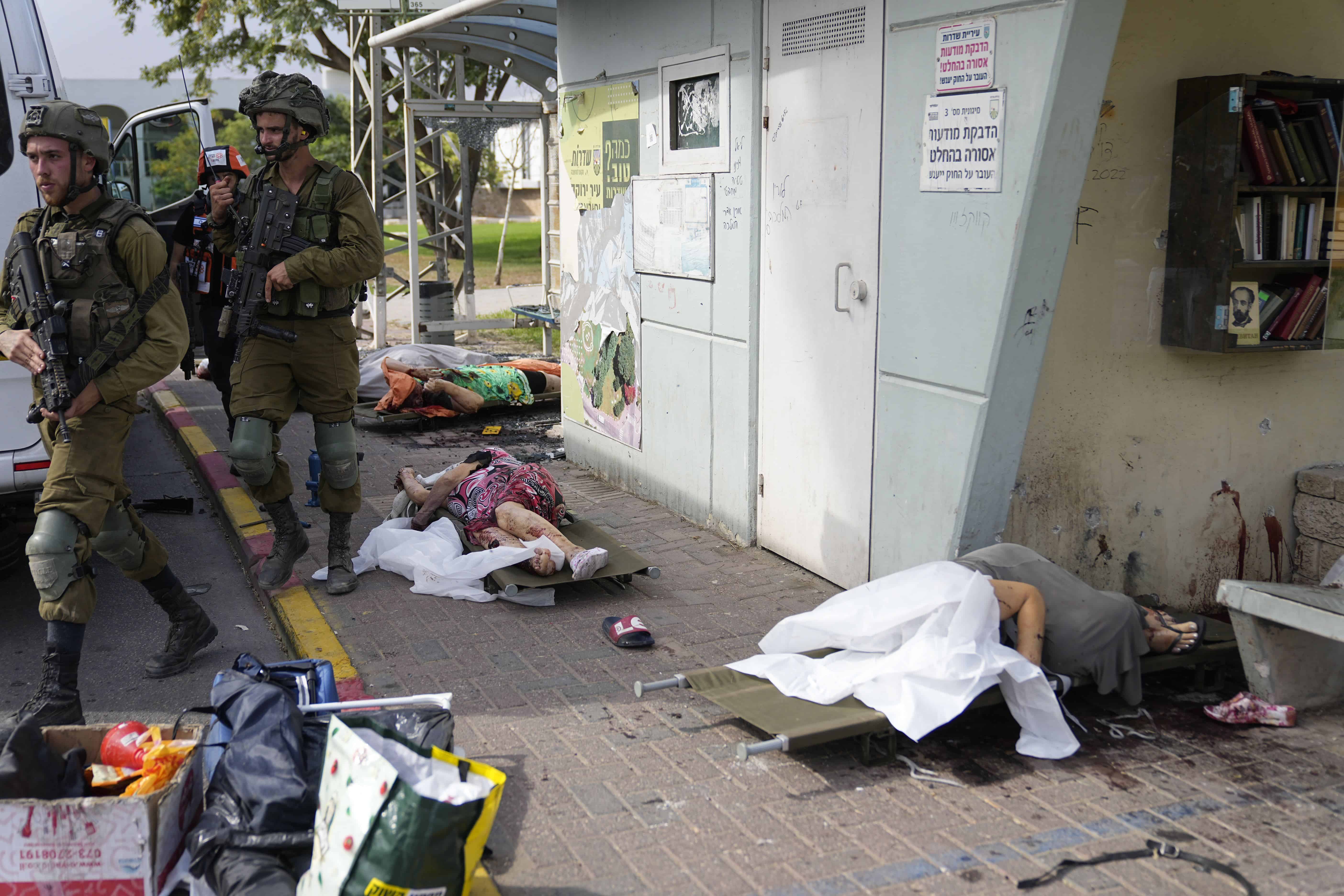 Soldados israelíes caminan junto a civiles asesinados por militantes palestinos en Sderot, Israel, el sábado 7 de octubre de 2023. Militantes palestinos en la Franja de Gaza se infiltraron el sábado en el sur de Israel y dispararon miles de cohetes contra el país mientras Israel comenzaba a atacar objetivos en Gaza. en respuesta.
