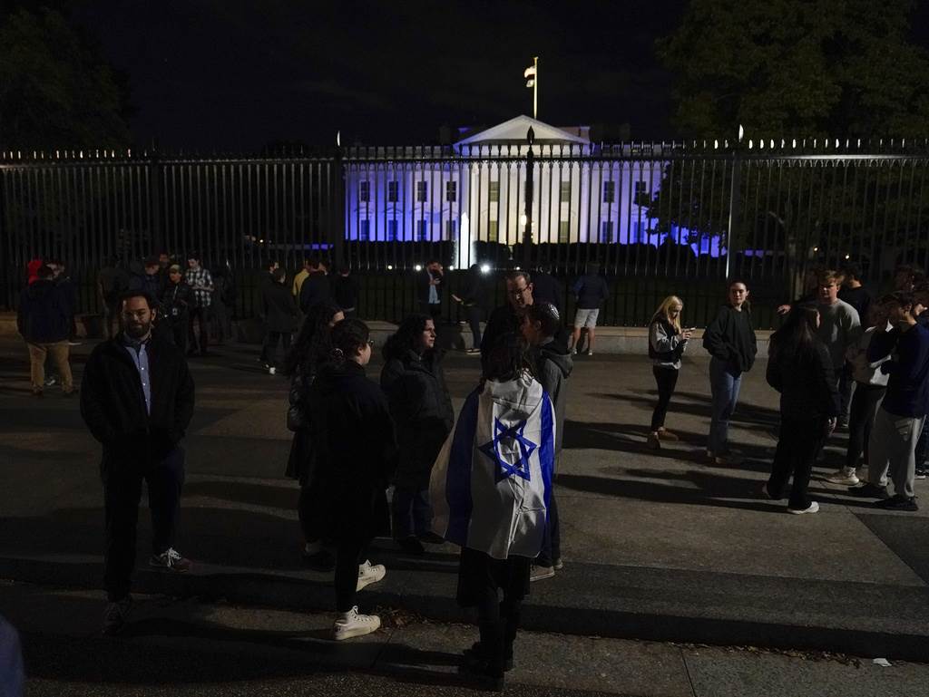 La gente se encuentra con una bandera israelí frente a la Casa Blanca, iluminada en azul y blanco para subrayar la solidaridad de Estados Unidos con Israel, el lunes 9 de octubre de 2023, en Washington.