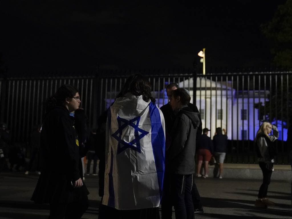 La gente se encuentra con una bandera israelí frente a la Casa Blanca, iluminada en azul y blanco para subrayar la solidaridad de Estados Unidos con Israel, el lunes 9 de octubre de 2023, en Washington.