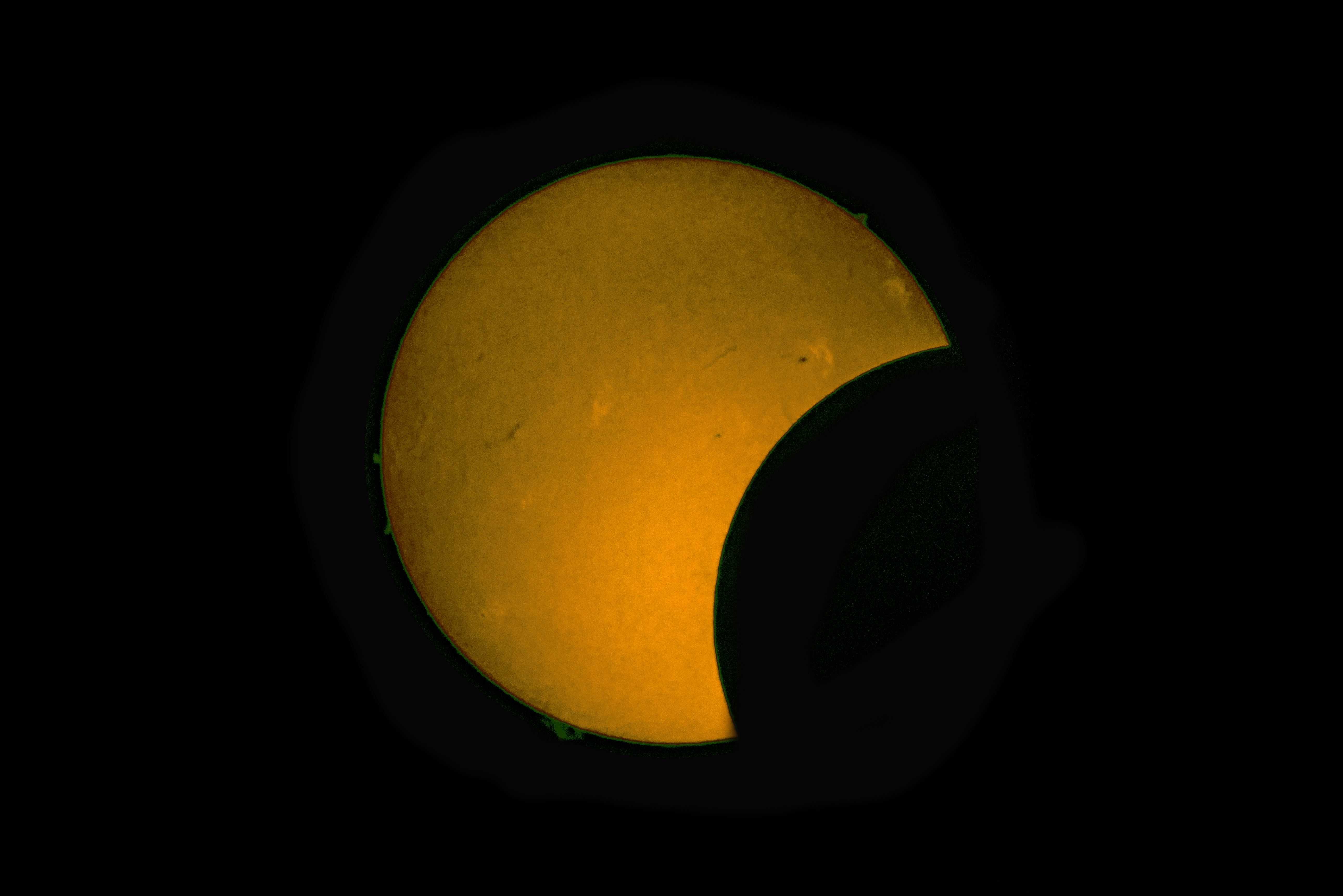 En la imagen se pueden apreciar diversos elementos de la cromosfera solar junto al borde la Luna, incluso se logran ver algunas llamaradas solares coloreadas en verde.