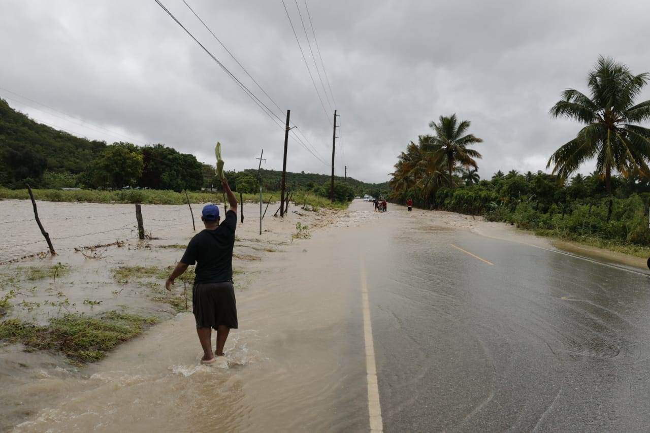 Un hombre hace señas para advertir a los conductores sobre la imposibilidad de continuar por la ruta a causa de las inundaciones.