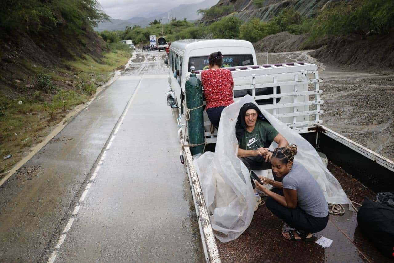 Cubriéndose de la lluvia, tres personas aguardan por el momento para cruzar un lodazal producto de las lluvias que azotan la región desde la madrugada.