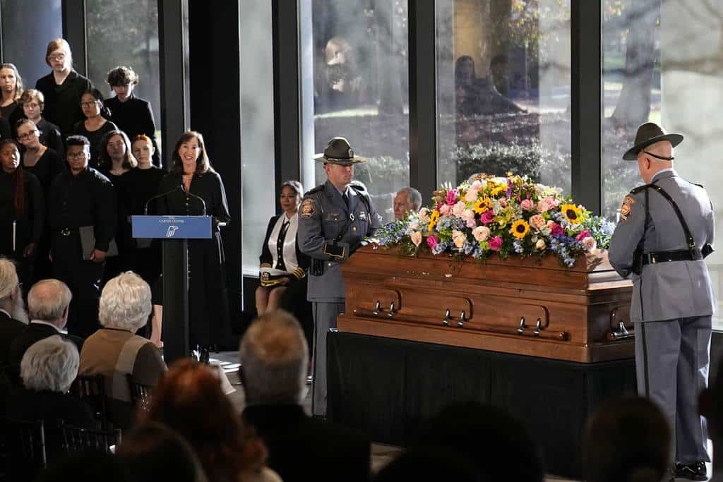 Miembros de la guardia de honor de la Patrulla Estatal de Georgia se paran en el ataúd de la ex primera dama Rosalynn Carter mientras Paige Alexander, directora ejecutiva de The Carter Center, habla durante un servicio de descanso en el vestíbulo de la Biblioteca y Museo Presidencial Jimmy Carter en Atlanta, el lunes 27 de noviembre de 2023.