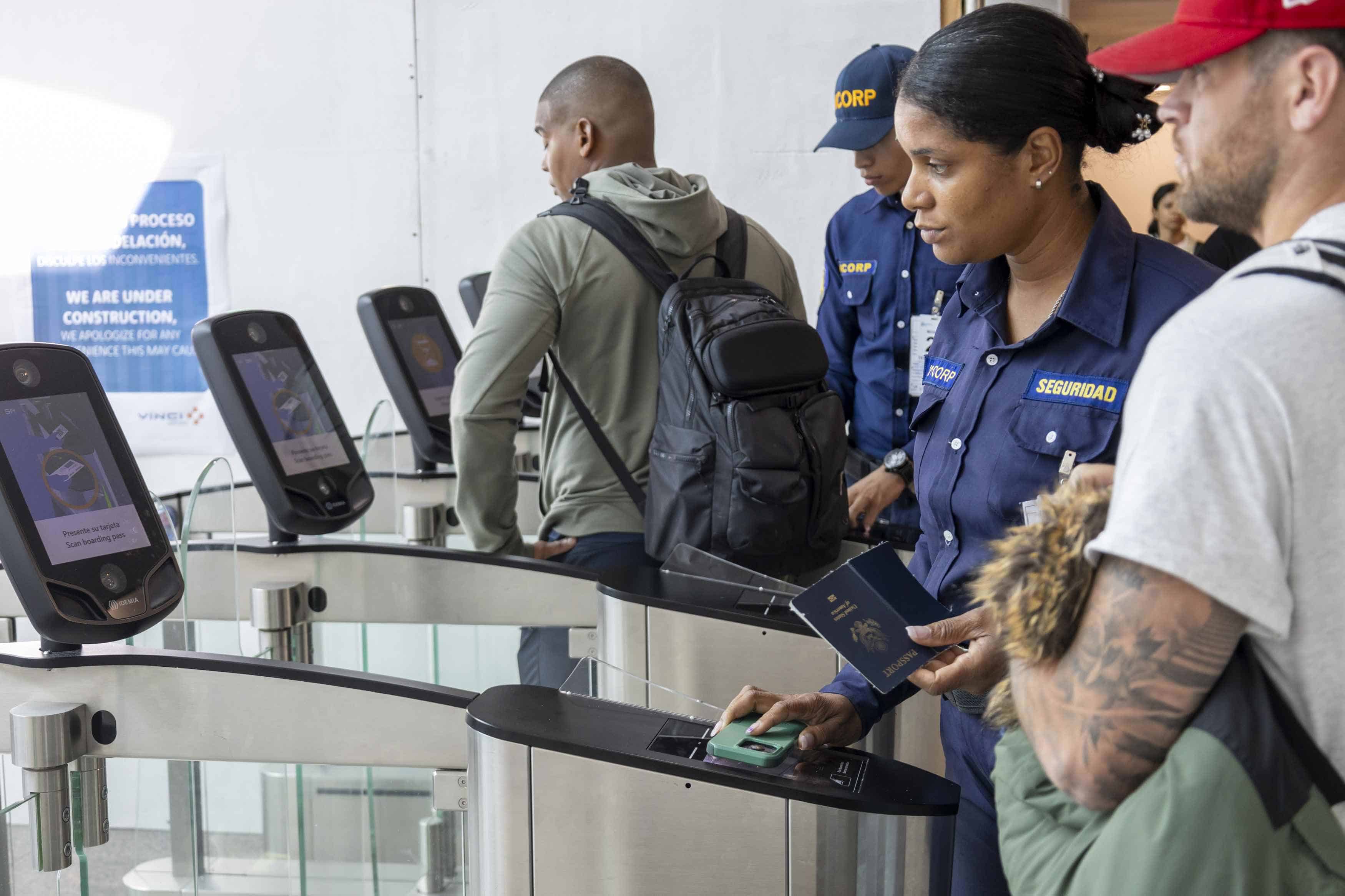 Una agente ayuda a un pasajero a escanear su pasaporte para acceder al área de migración.