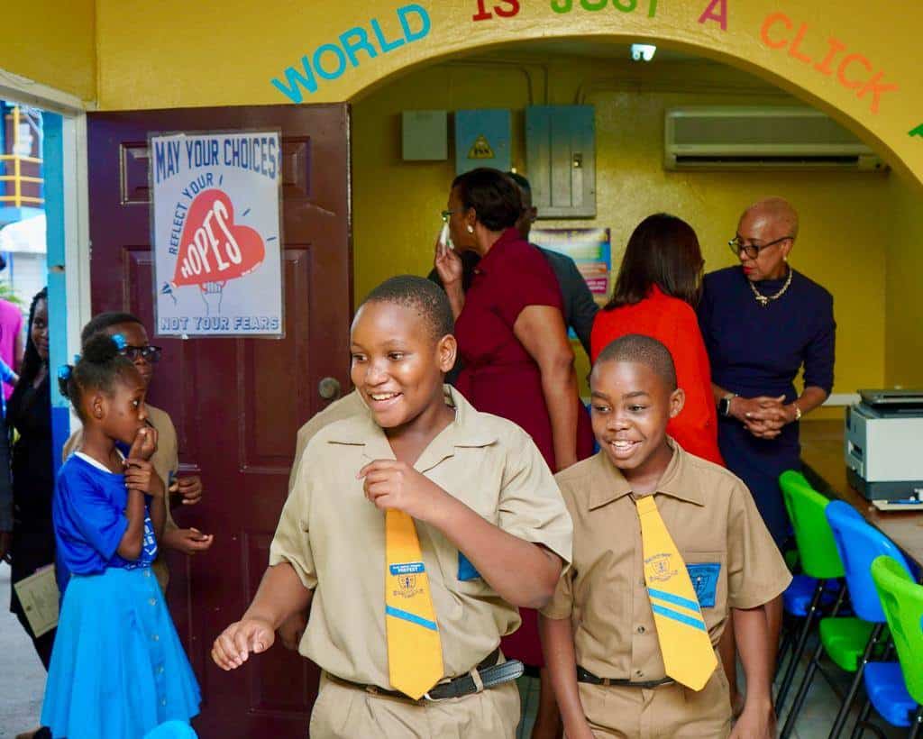 Niños de la Escuela Primaria Clan Carthy entran corriendo y riendo al aula de informática. 