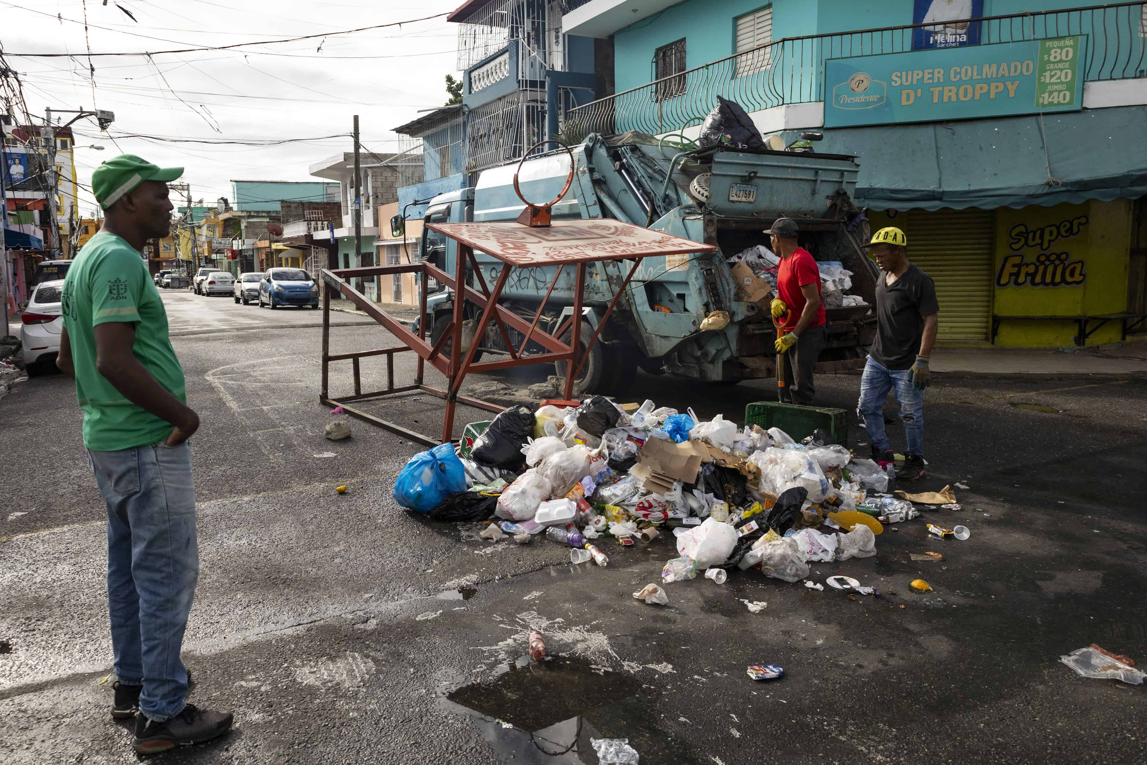 Trabajadores de un camión recolector de desechos sólidos miran como la basura y un tablero de baloncesto ocupan los espacios de la calle Luis Reyes Acosta, en el barrio 27 de Febrero.