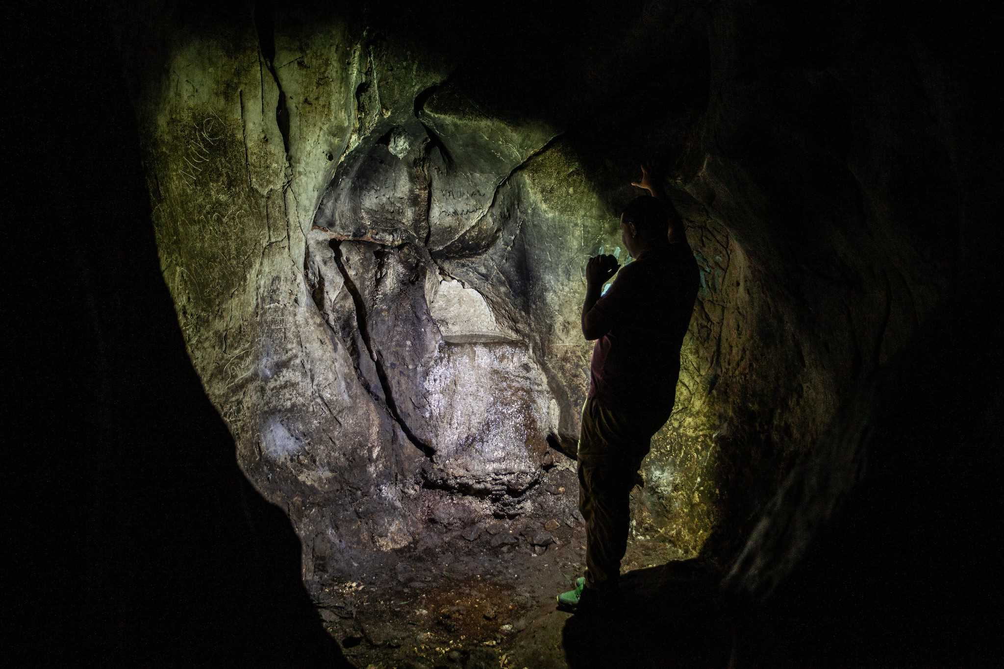Timoteo Estévez alumbra con una linterna el pequeño pozo que da nombre a la cueva.<br>