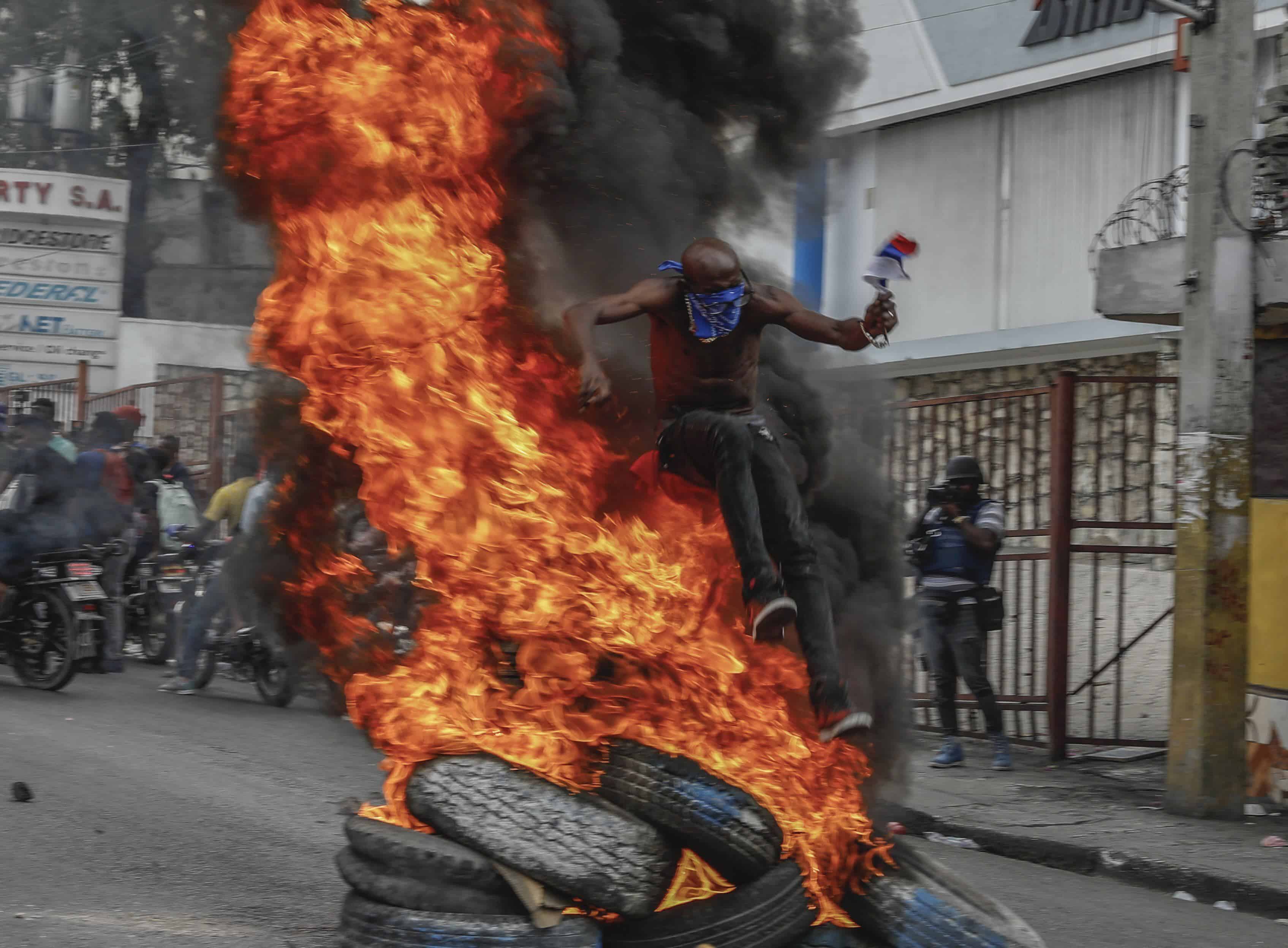 Un manifestante brinca por encima de neumáticos en llamas durante una protesta contra el primer ministro haitiano Ariel Henry, el lunes 5 de febrero de 2024, en Puerto Príncipe.
