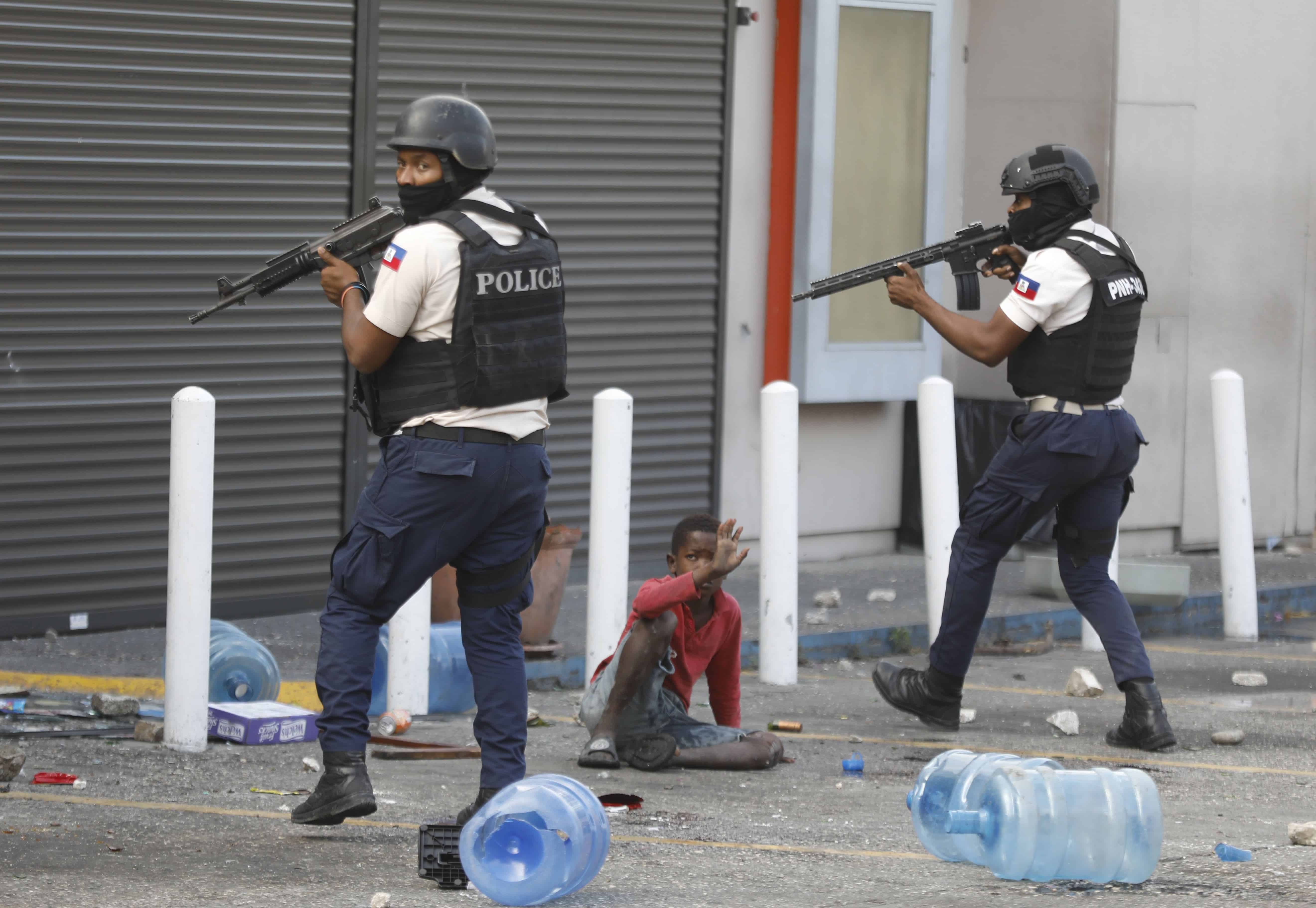 Un niño levanta el brazo de manera protectora mientras la policía se prepara para entrar en una tienda de comestibles destrozada, durante una protesta para exigir la renuncia del Primer Ministro Ariel Henry en el barrio de Petion-Ville de Puerto Príncipe, Haití, el martes 6 de febrero 2024.