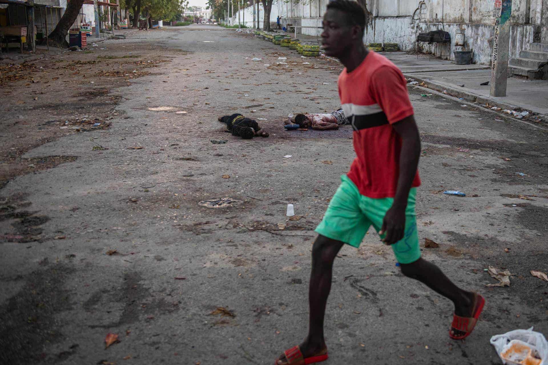 Un hombre pasa frente unos cadáveres este domingo, en una calle de Puerto Príncipe (Haití). Al menos una decena de personas murió tras el ataque anoche a la prisión civil de Puerto Príncipe por parte de bandas armadas, que habrían liberado a numerosos delincuentes importantes durante su asalto al presidio.