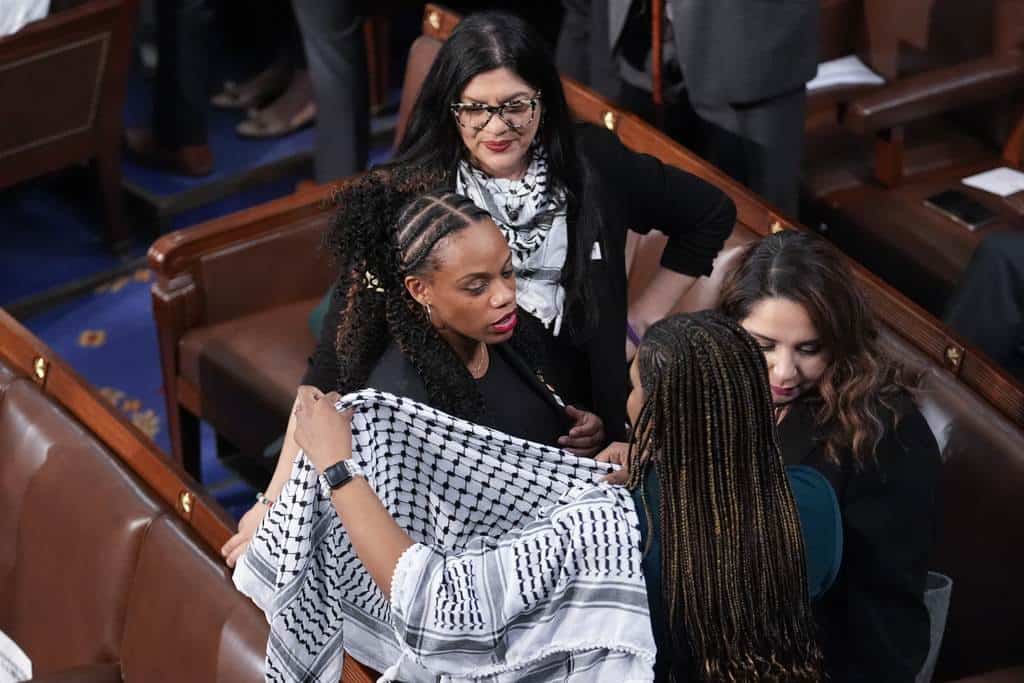 La representante Summer Lee, demócrata de Pensilvania, se pone una bufanda, mientras la representante Rashida Tlaib, demócrata de Michigan, arriba, observa, antes de que el presidente Joe Biden llegue para pronunciar su discurso sobre el Estado de la Unión en una sesión conjunta del Congreso, en el Capitolio en Washington, el jueves 7 de marzo de 2024.