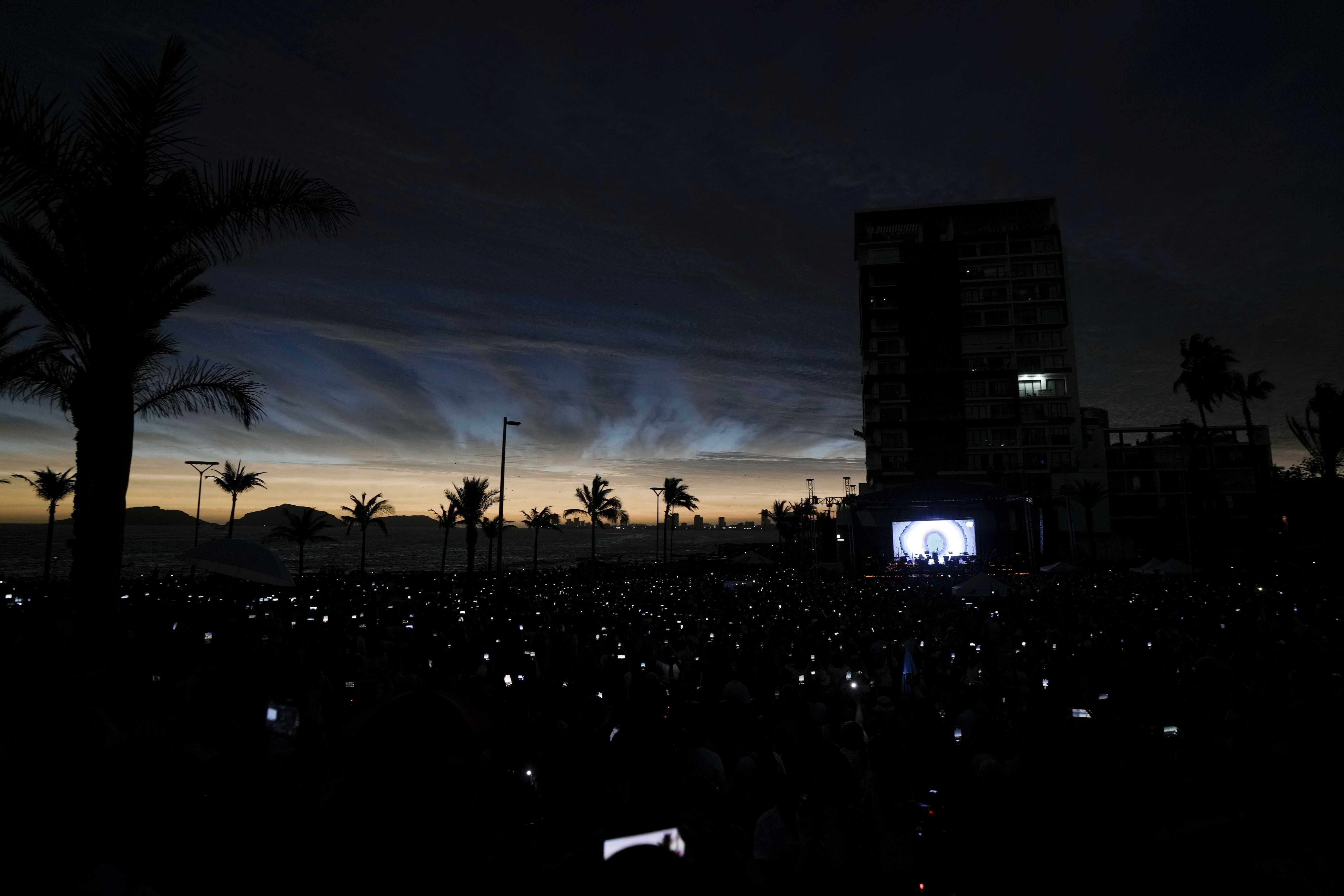La gente usa sus teléfonos celulares mientras el cielo se oscurece durante un eclipse solar total en Mazatlán, México, el lunes 8 de abril de 2024.