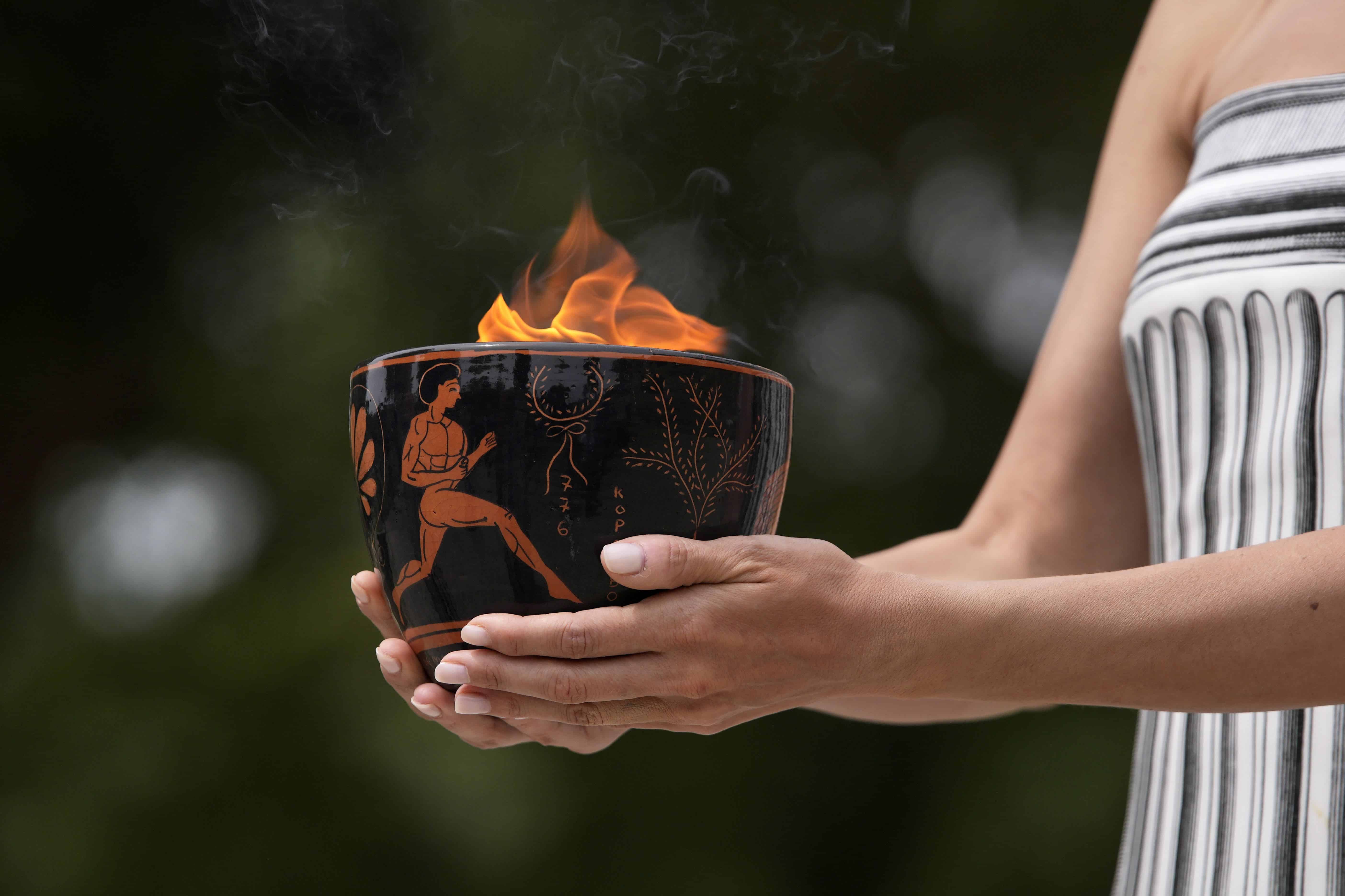 Un artista sostiene una vasija de cerámica con la llama durante la ceremonia oficial de encendido de la llama de los Juegos Olímpicos de París, en el sitio de la Antigua Olimpia, Grecia.