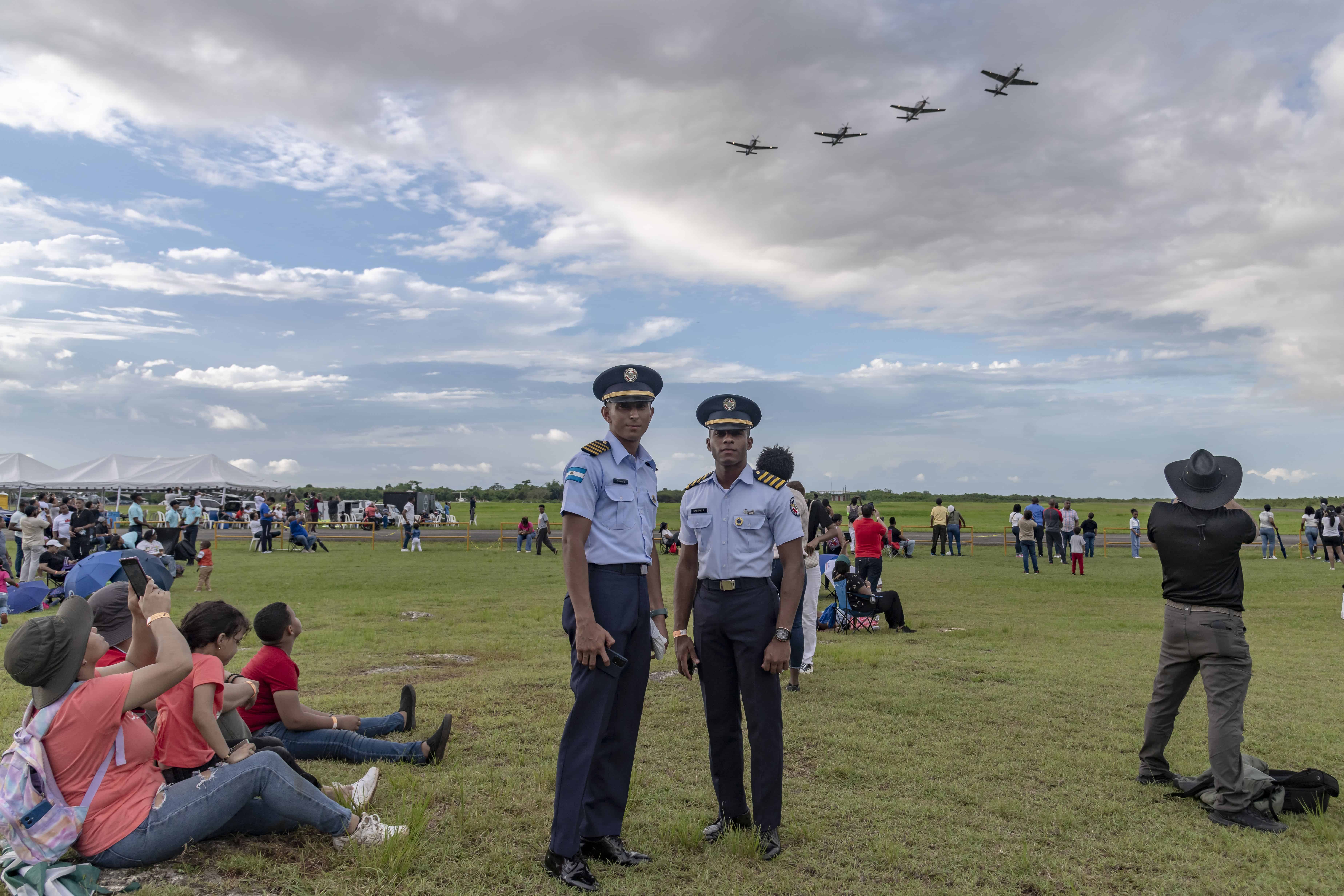 Dos cadetes de la academia posan, mientras detrás pasa una formación de aviones Super Tucano, máximo exponente de la fuerza aérea.