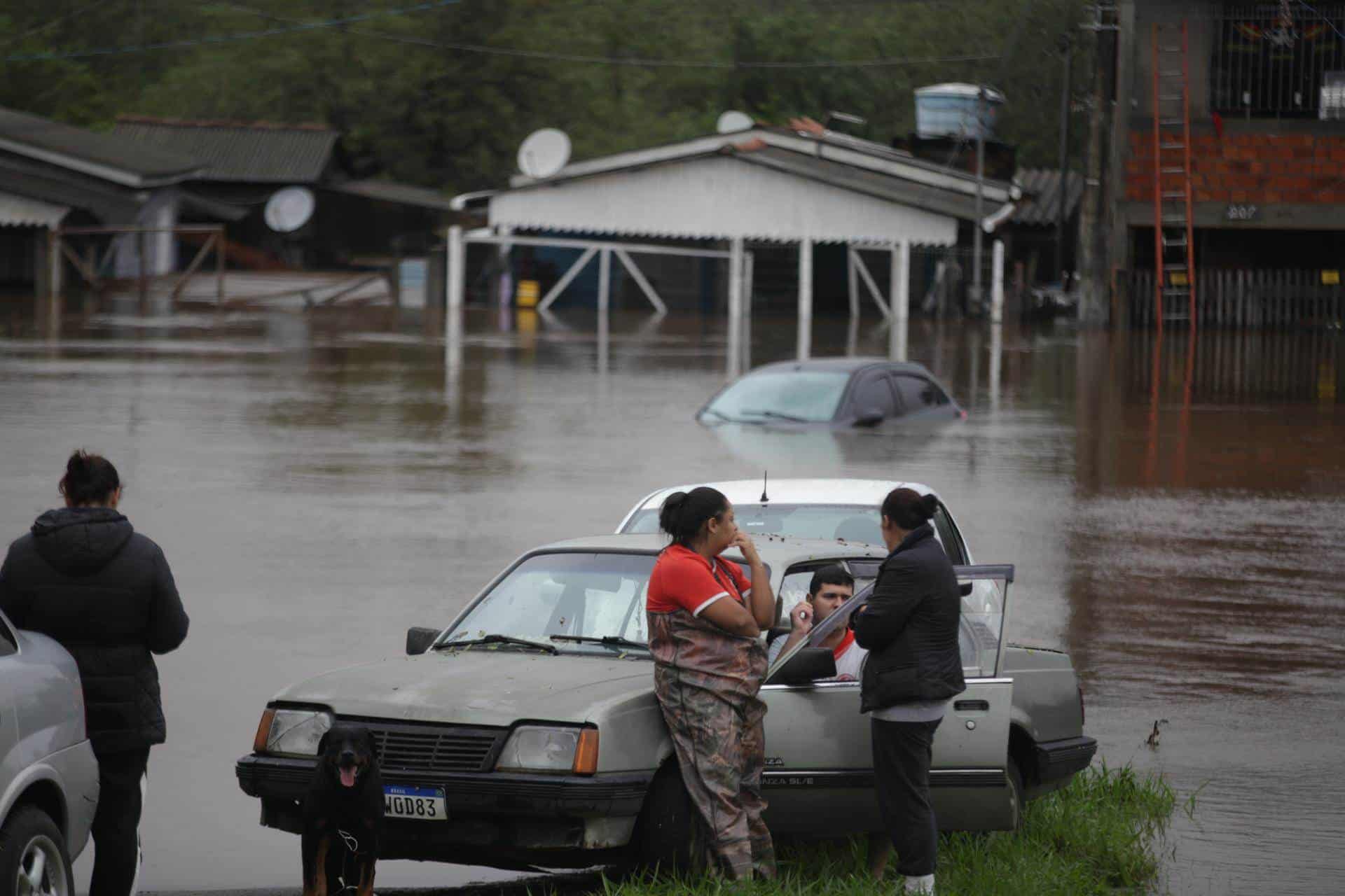 Varias personas esperan junto a unos vehículos atrapados en una zona inundada por las lluvias este viernes, en Porto Alegre (Brasil). 