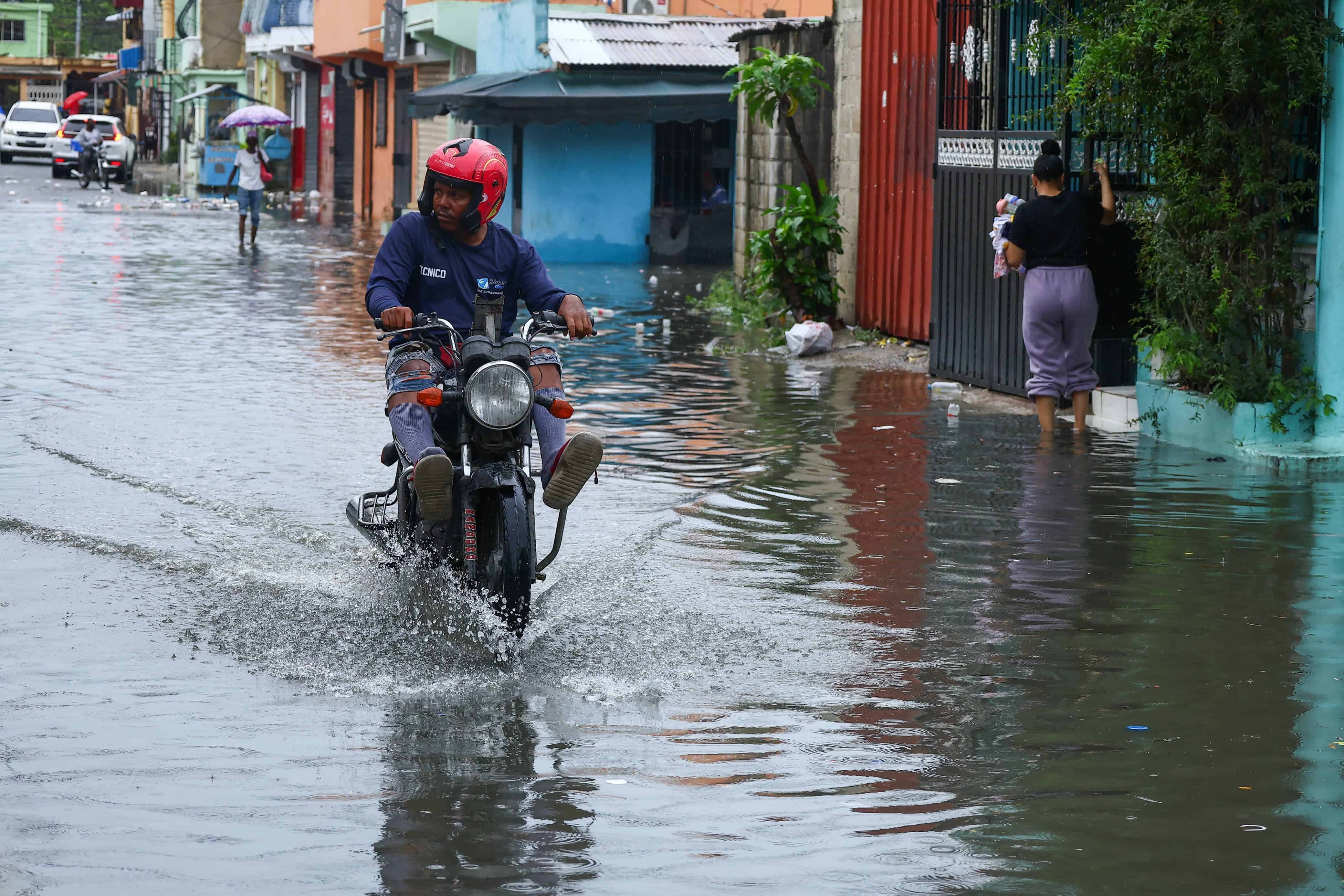 Un motorista eleva sus pies para cruzar una calle de Santo Domingo Este anegada por las lluvias producto de la vaguada que afecta el territorio nacional.