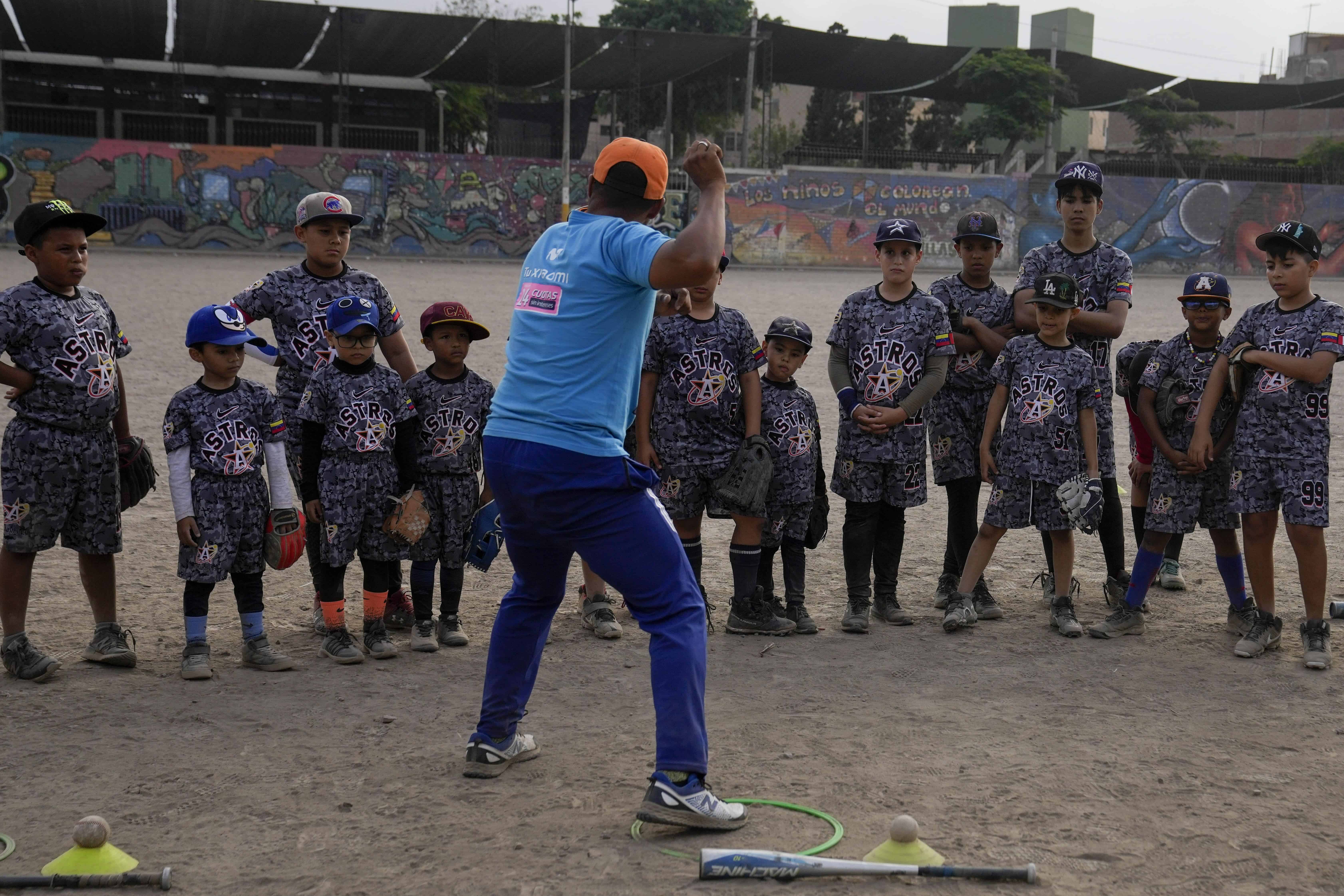 El entrenador de béisbol Franklin López muestra a jóvenes inmigrantes venezolanos cómo lanzar una pelota durante una sesión de práctica de béisbol en un parque público en el área de Comas, en las afueras de Lima, Perú, el 2 de mayo de 2024.