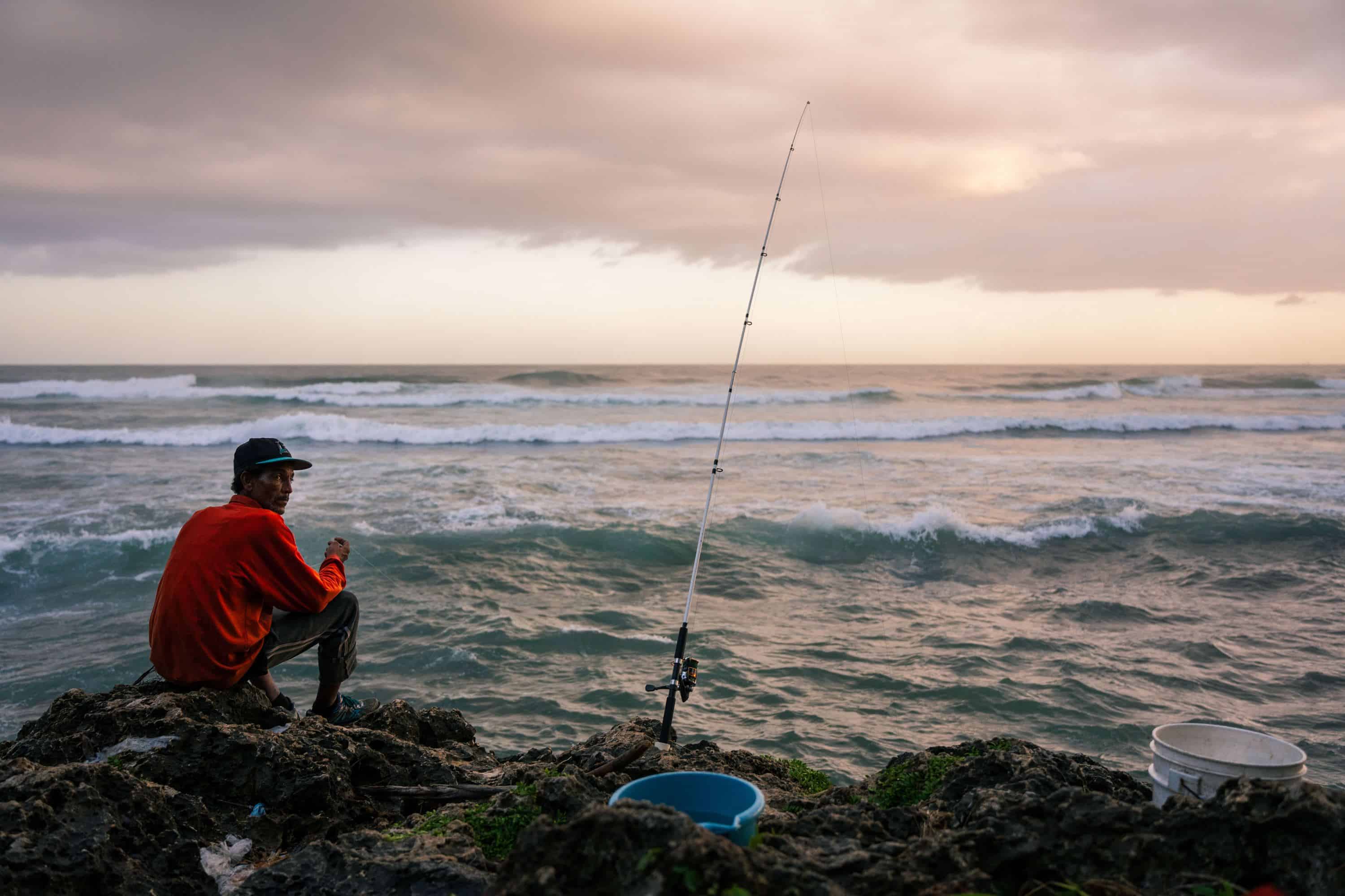 Categoría Retrato: Primer lugar. Un hombre pesca en el Malecón de Santo Domingo. Cada día, cientos de pescadores llegan antes del amanecer y permanecen hasta el anochecer, incluso bajo la lluvia, especialmente en la Plaza Juan Varón en Santo Domingo.Esta imagen captura la perseverancia y la dedicación de los pescadores que, día tras día, enfrentan las adversidades para ganarse la vida.