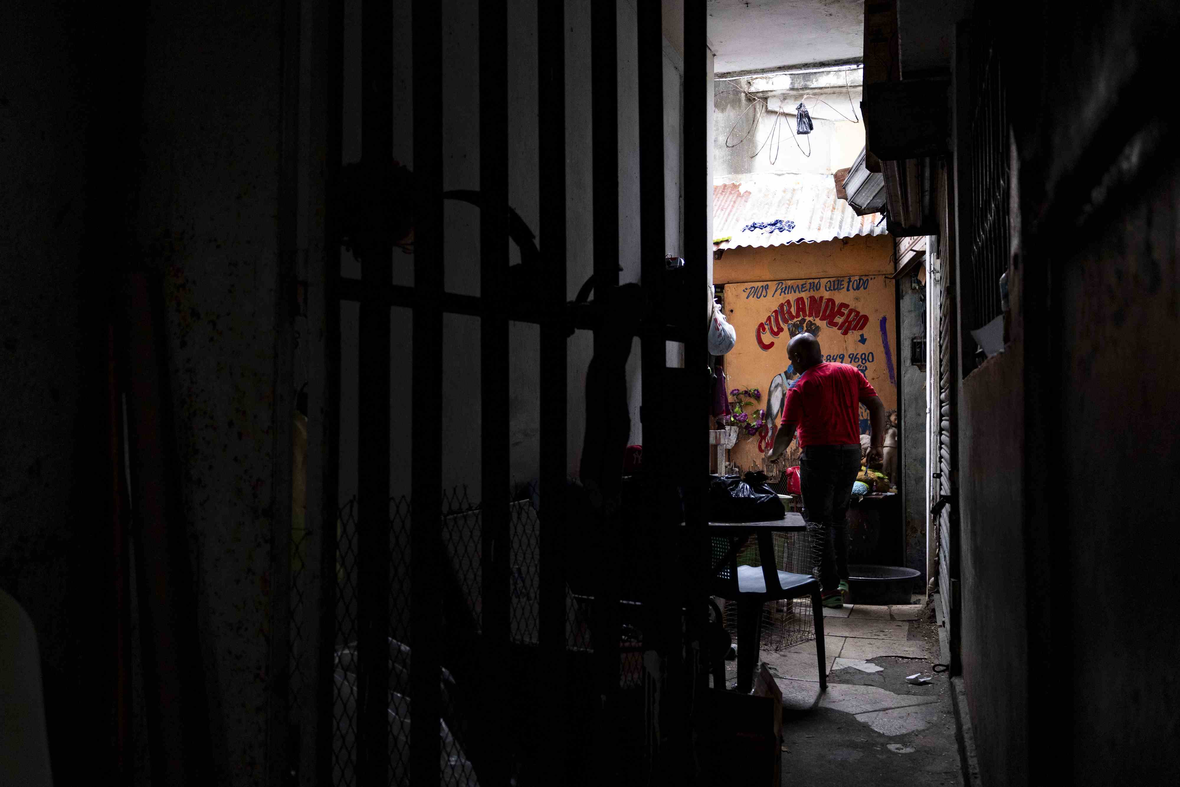 El curandero Rodolfo, caminando antes de leer las cartas, bajo unas letras en la pared que indican: curandero.