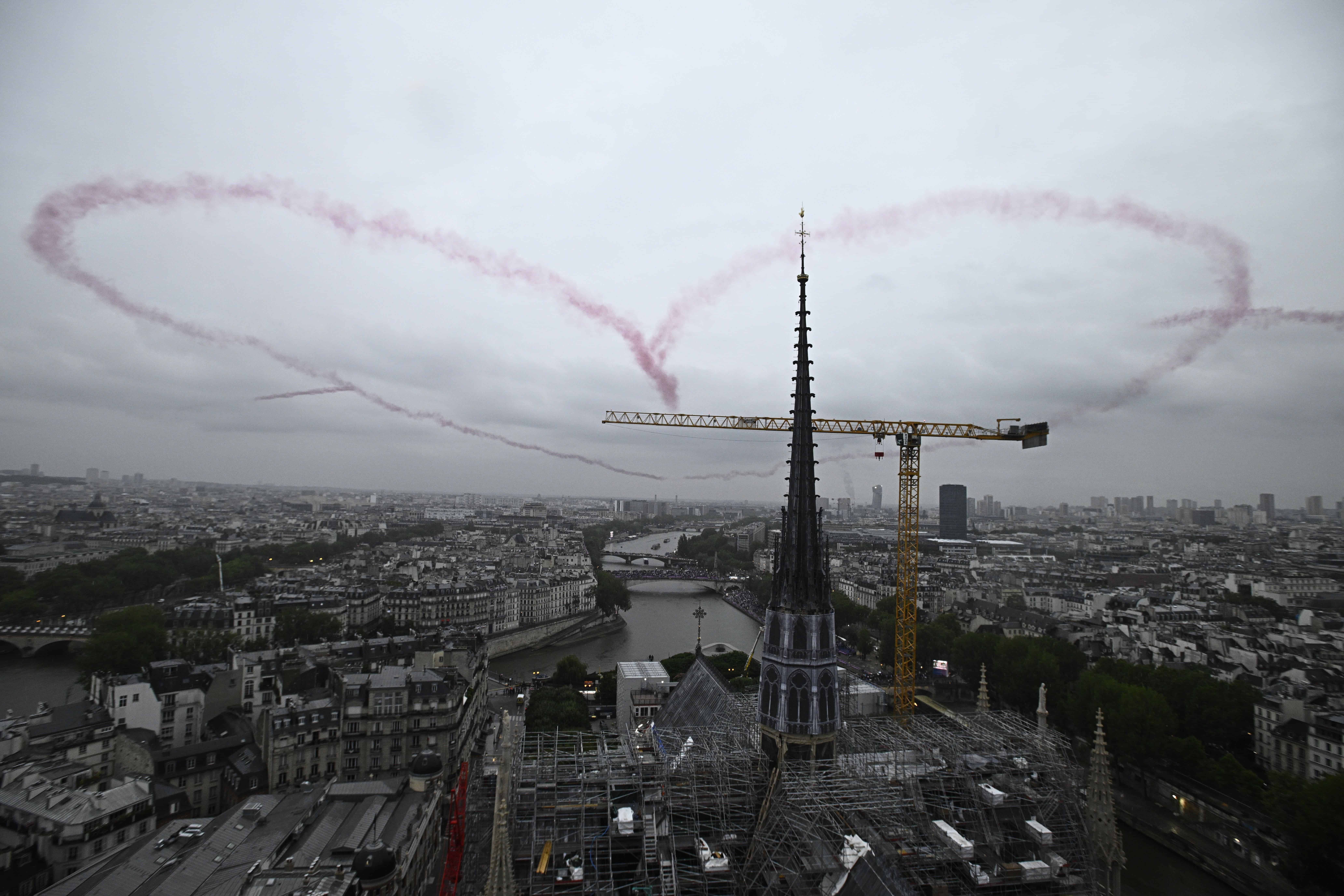 Un corazón hecho con humo rojo por cuatro aviones flota en el aire cerca de la Catedral de Notre-Dame en París, Francia, durante la ceremonia de apertura de los Juegos Olímpicos de Verano de 2024, el viernes 26 de julio de 2024.